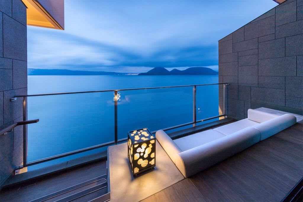 A terrace onsen above Lake Toya at dusk, the water and the far shore beyond the rail