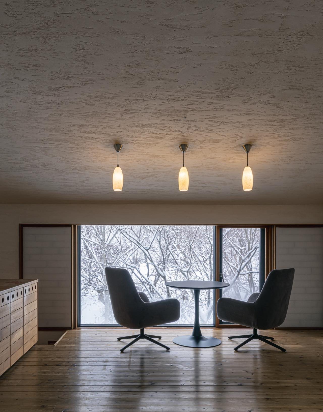 Two armchairs and a round table before a wide window onto trees, in a room at Kuramure