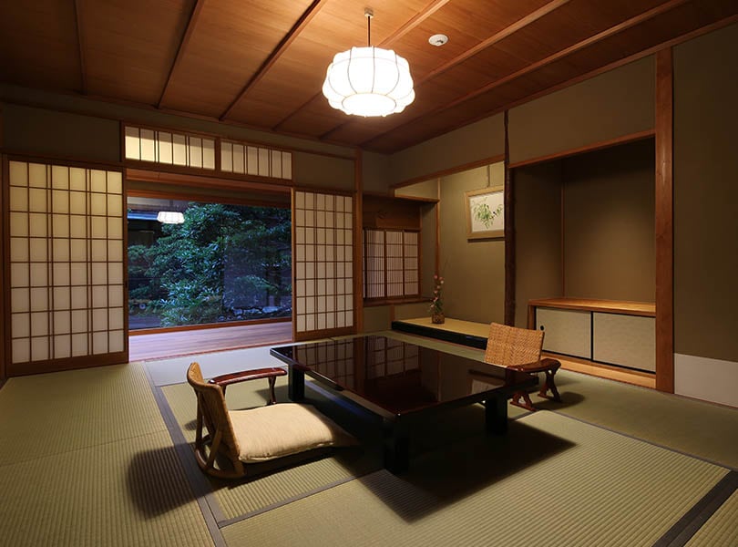 A tatami room with a lacquered table, the shoji drawn back to a window onto the trees