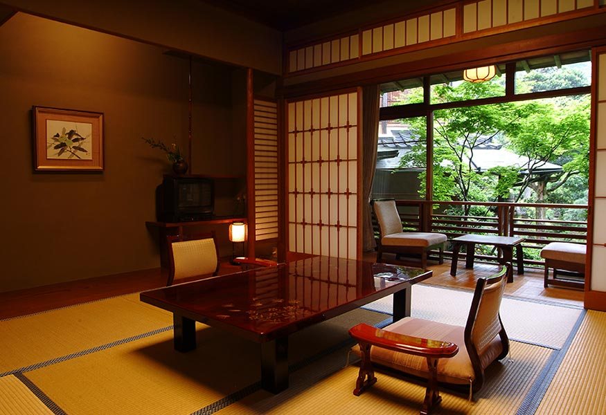 A tatami room with a lacquered table and low chairs, the shoji open to a veranda and the green of the garden