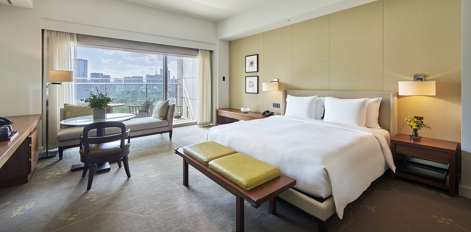 A room at Palace Hotel Tokyo, a wide bed and a sofa by a long window onto the palace gardens