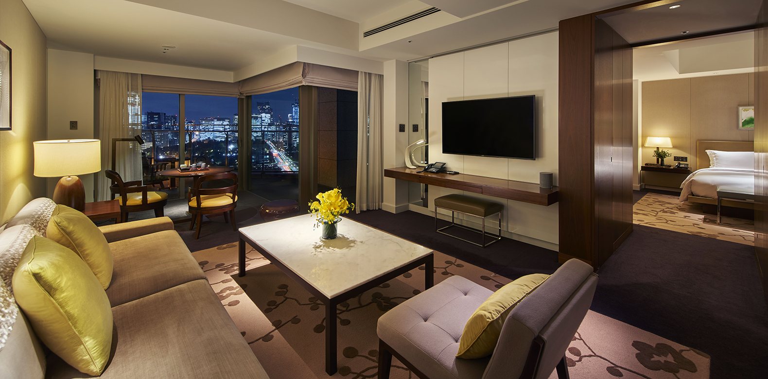 The living room of an executive suite in the evening, a sofa and armchairs before a window onto the lit city