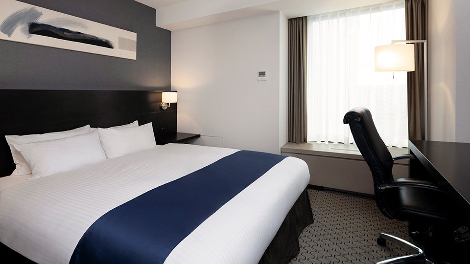 An executive room at the Sapporo Grand Hotel, a wide bed with a navy runner and a desk by a tall window
