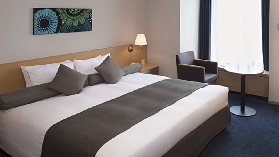 A double room with a deep blue carpet, an armchair and a small table by the window