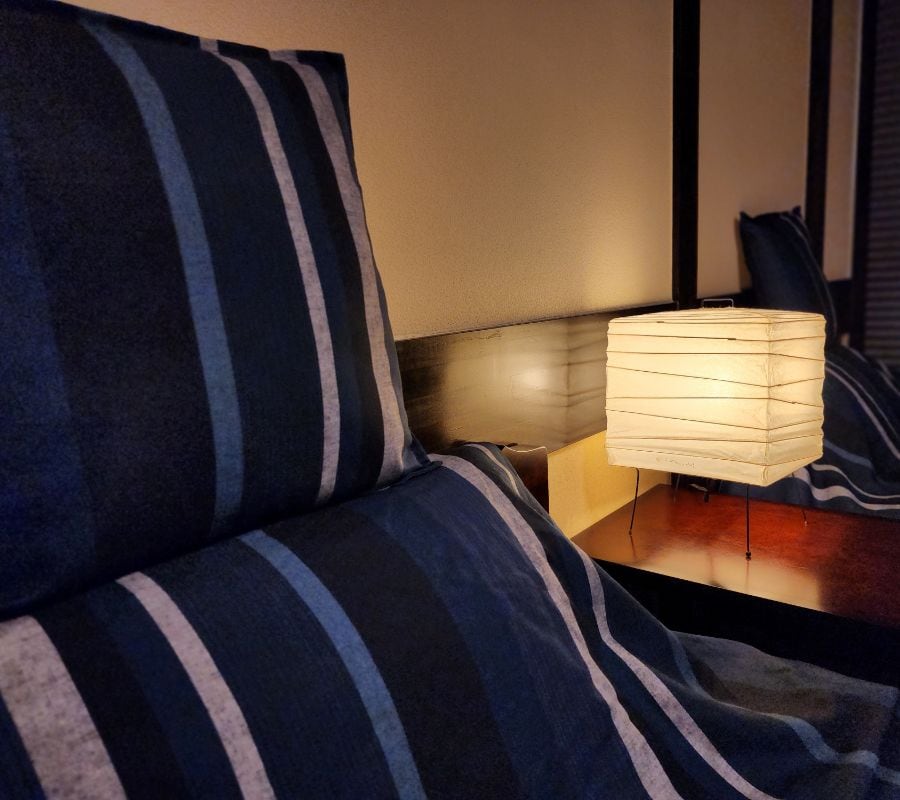 An indigo-striped cushion and a paper lantern glowing on a wooden headboard