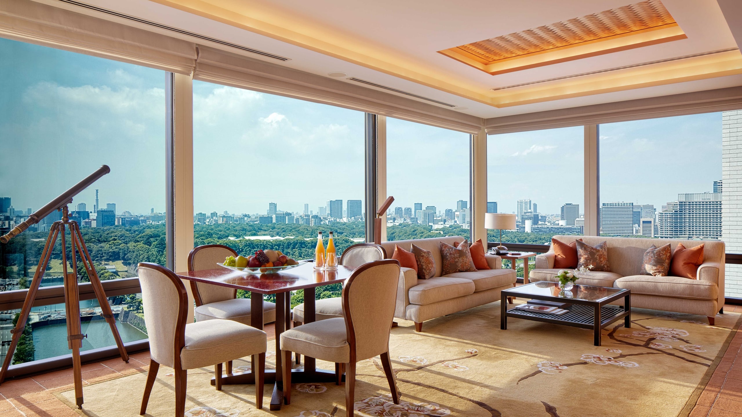 A suite living room in a corner of tall windows over the park and the city, a telescope at the glass
