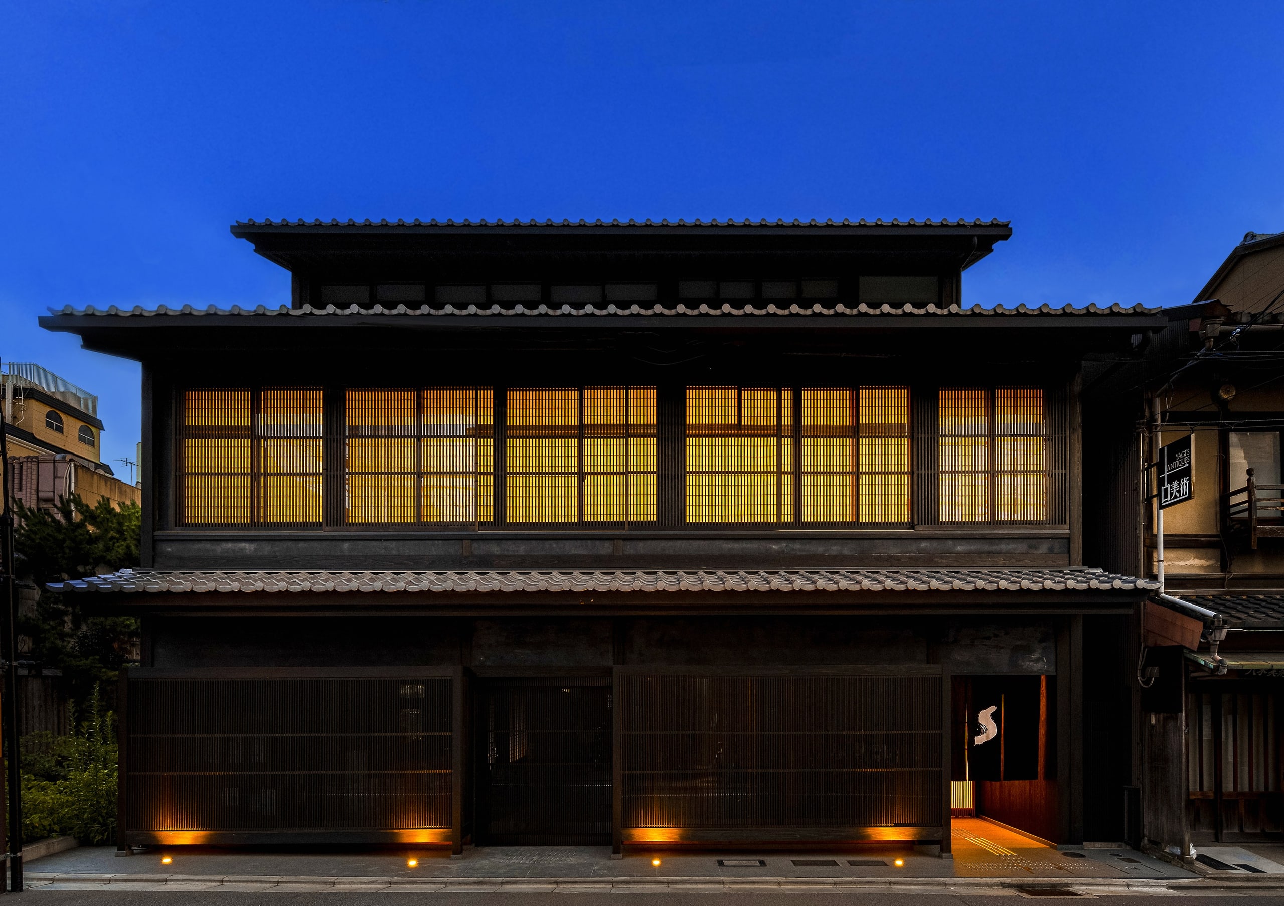 The timber front of the hotel on Shinmonzen Street, its lattice windows lit amber beneath a deep blue sky