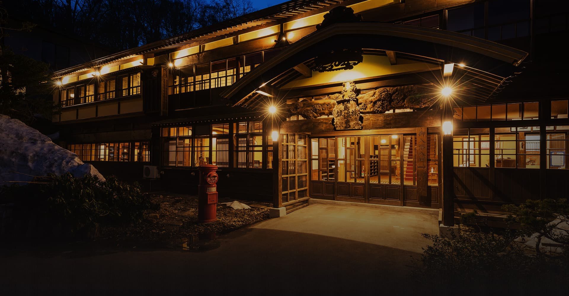The wooden inn of Tsuta Onsen lit at night among the beech forest