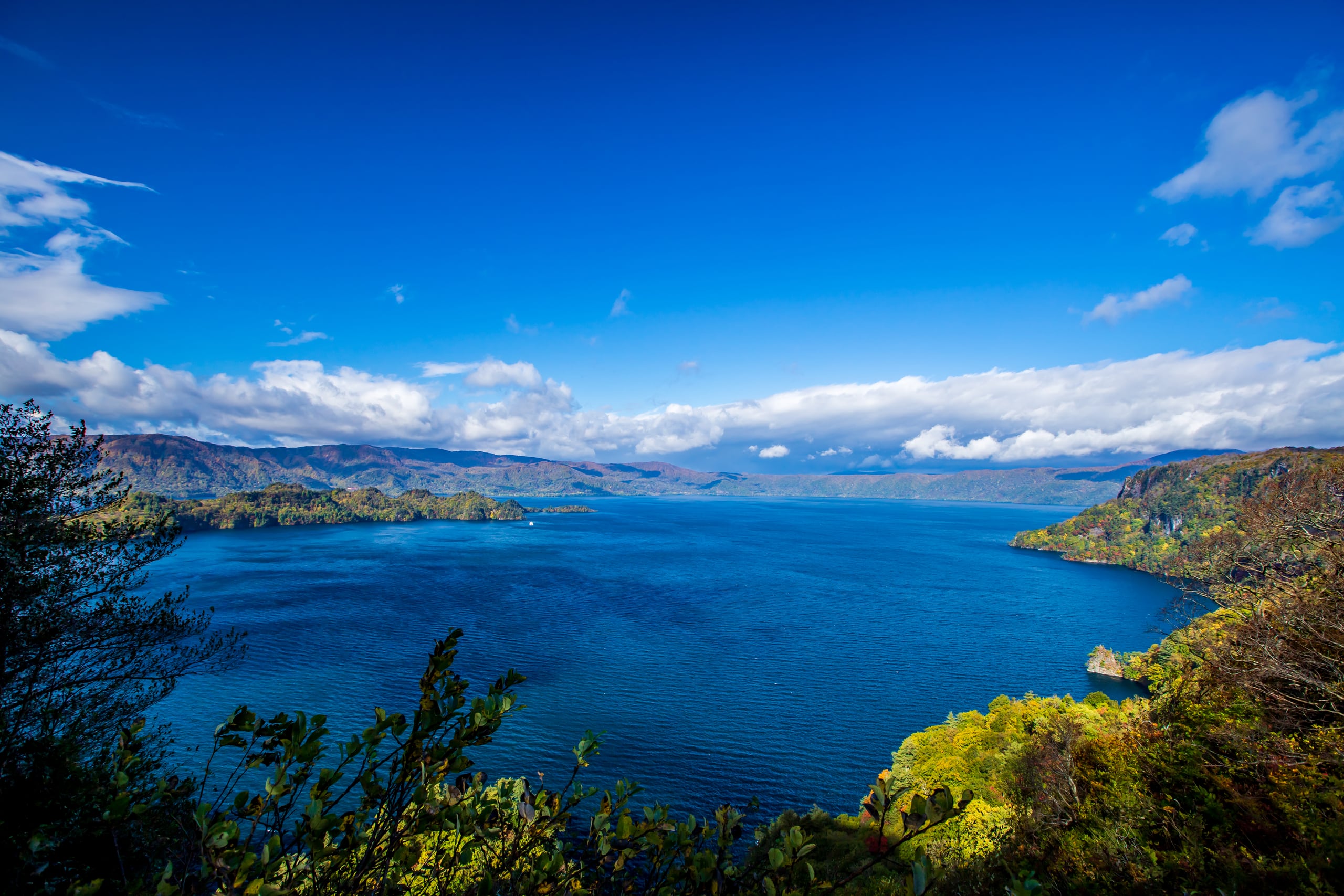 The deep blue water of Lake Towada seen from a height, forested headlands reaching into it