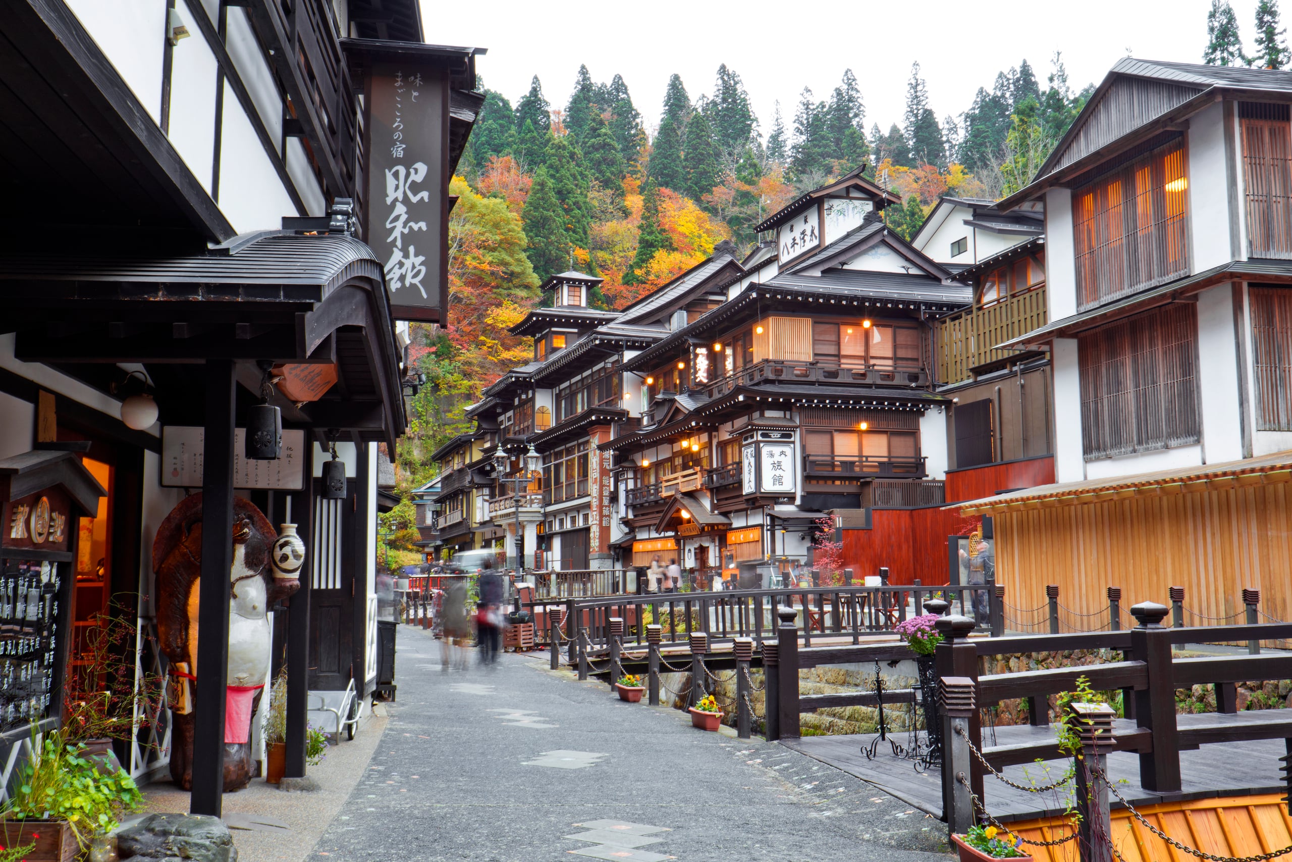 Multi-storey dark timber inns along the river street of Ginzan Onsen beneath autumn trees