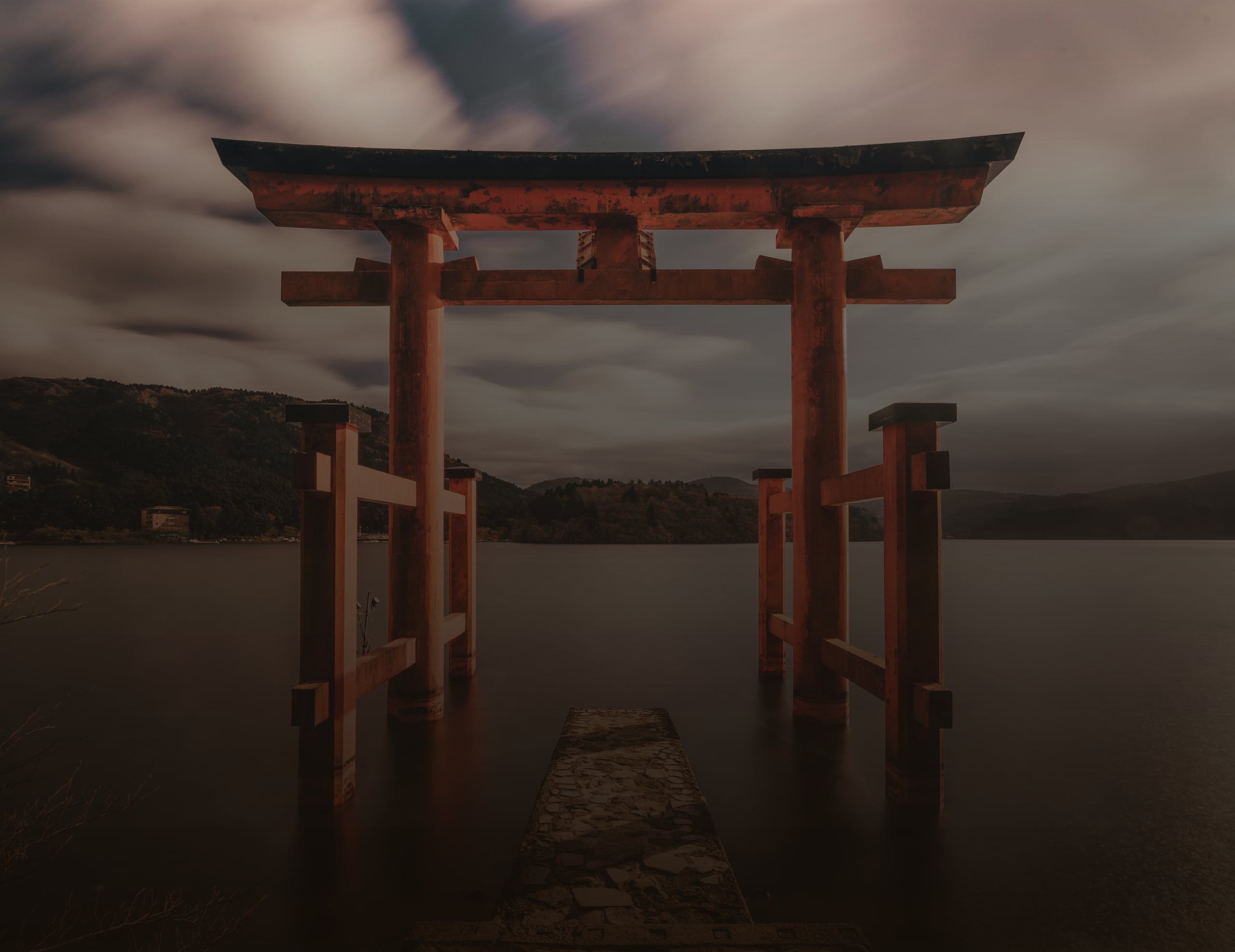 The red torii of Hakone Shrine standing in the calm water of Lake Ashi beneath grey cloud