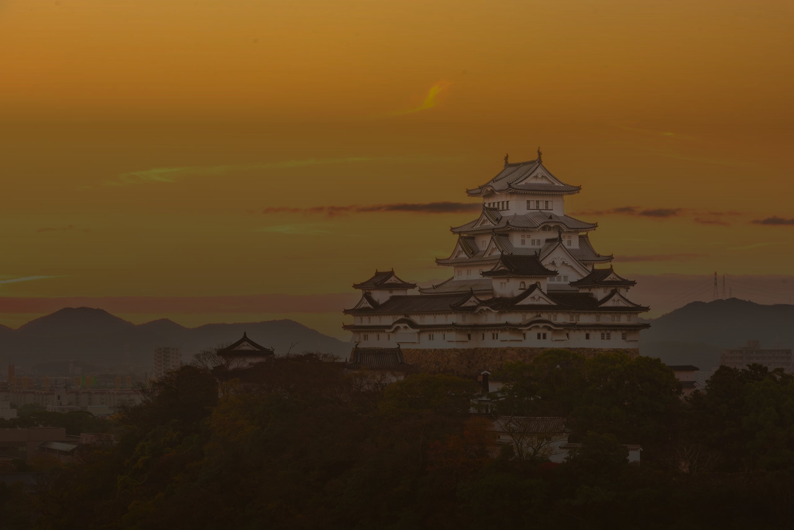 The white tiered keep of Himeji Castle above trees against an orange evening sky