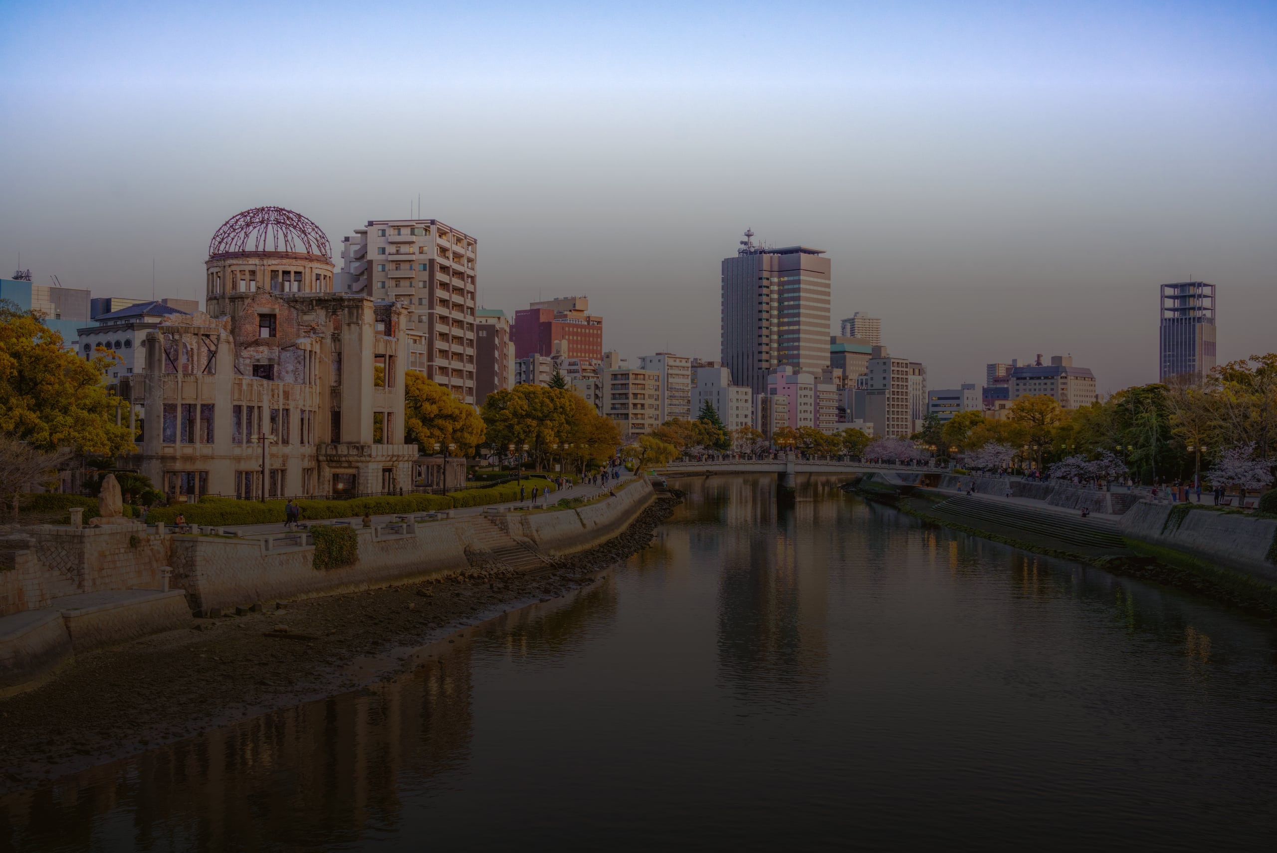 The Atomic Bomb Dome beside the Ota River at dusk, the city skyline reflected in the water
