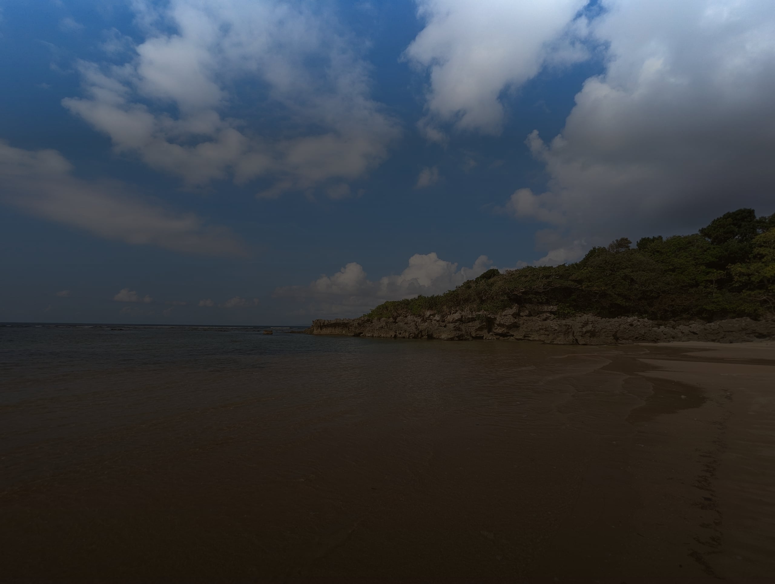 A cove of pale sand and clear shallow water beneath a green headland on the north coast of Ishigakijima