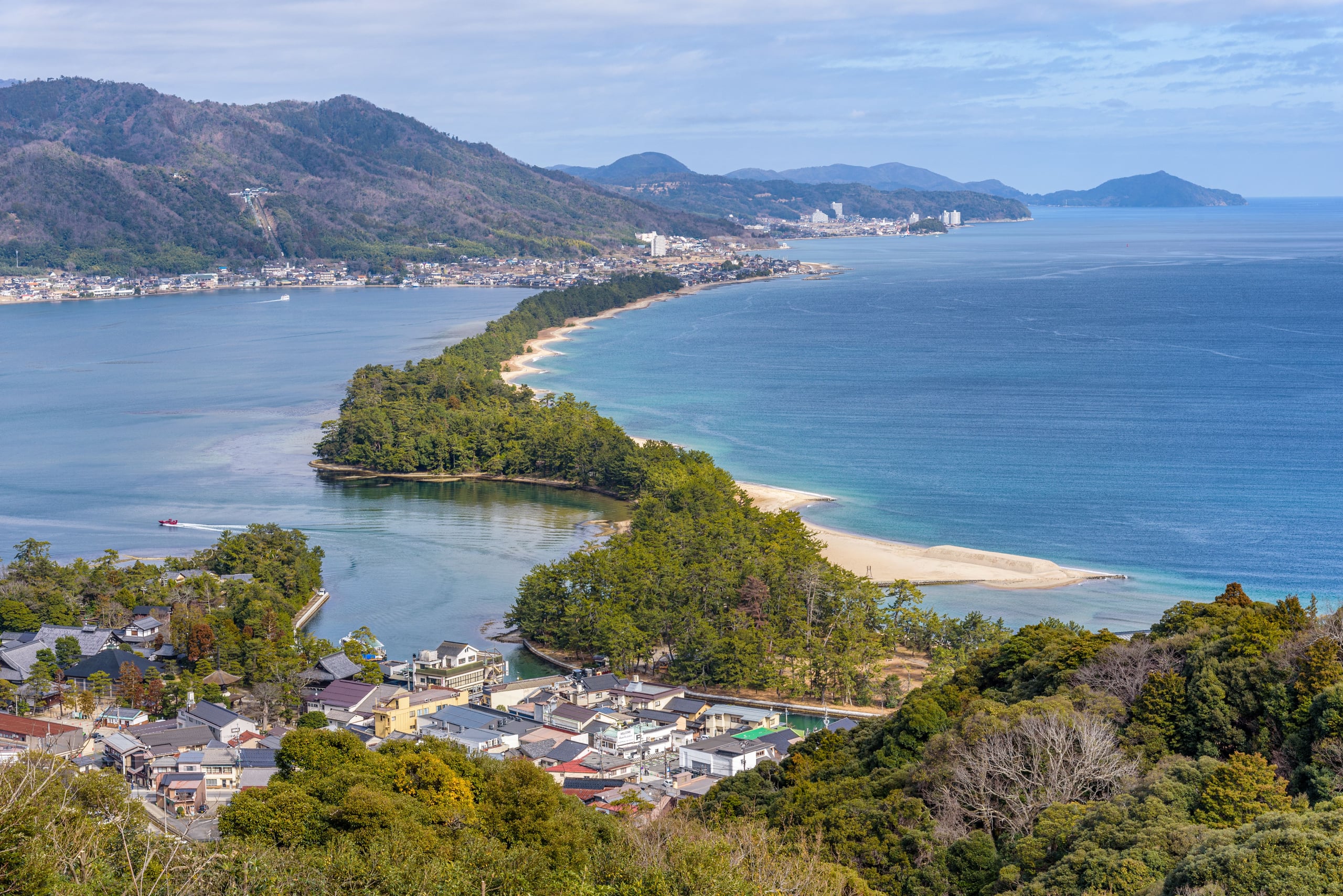 The pine-covered sandbar of Amanohashidate curving across Miyazu Bay on a clear day, seen from above