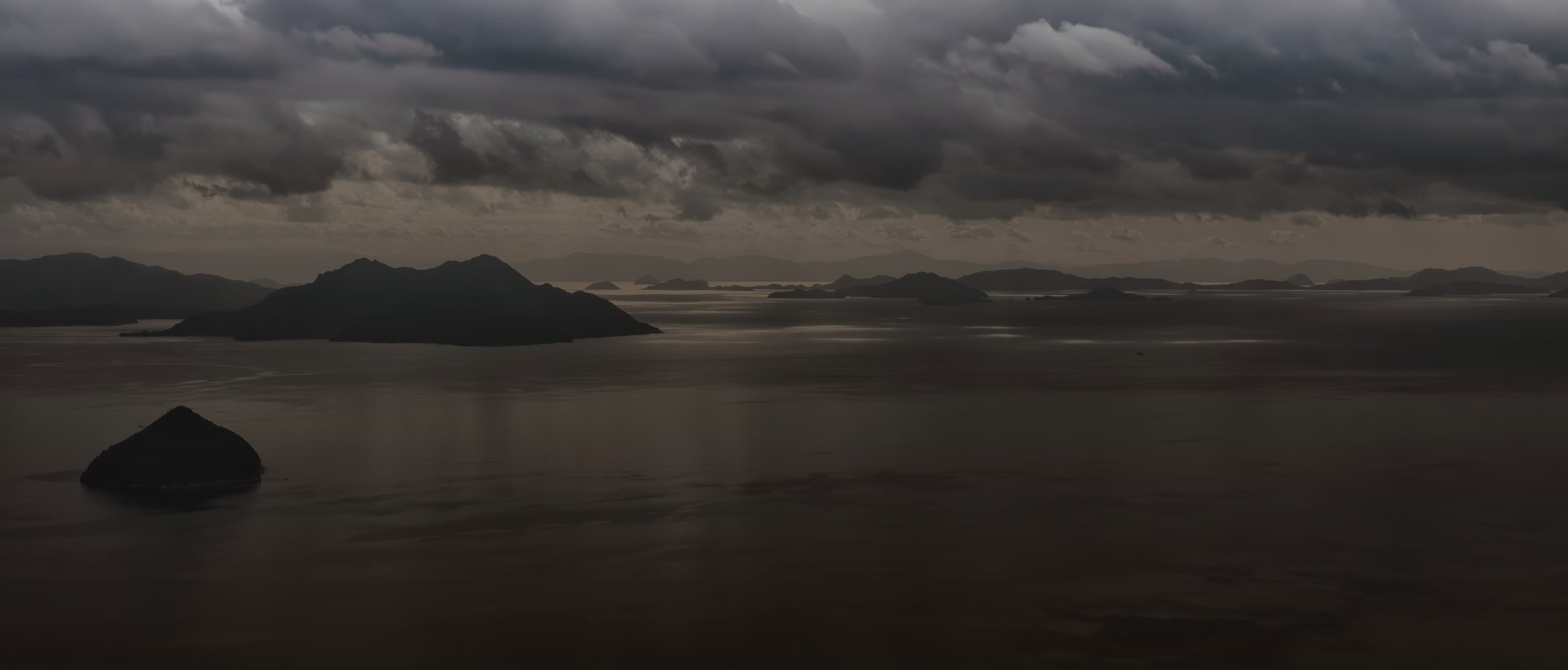 Low islands silhouetted on a calm sea under evening cloud