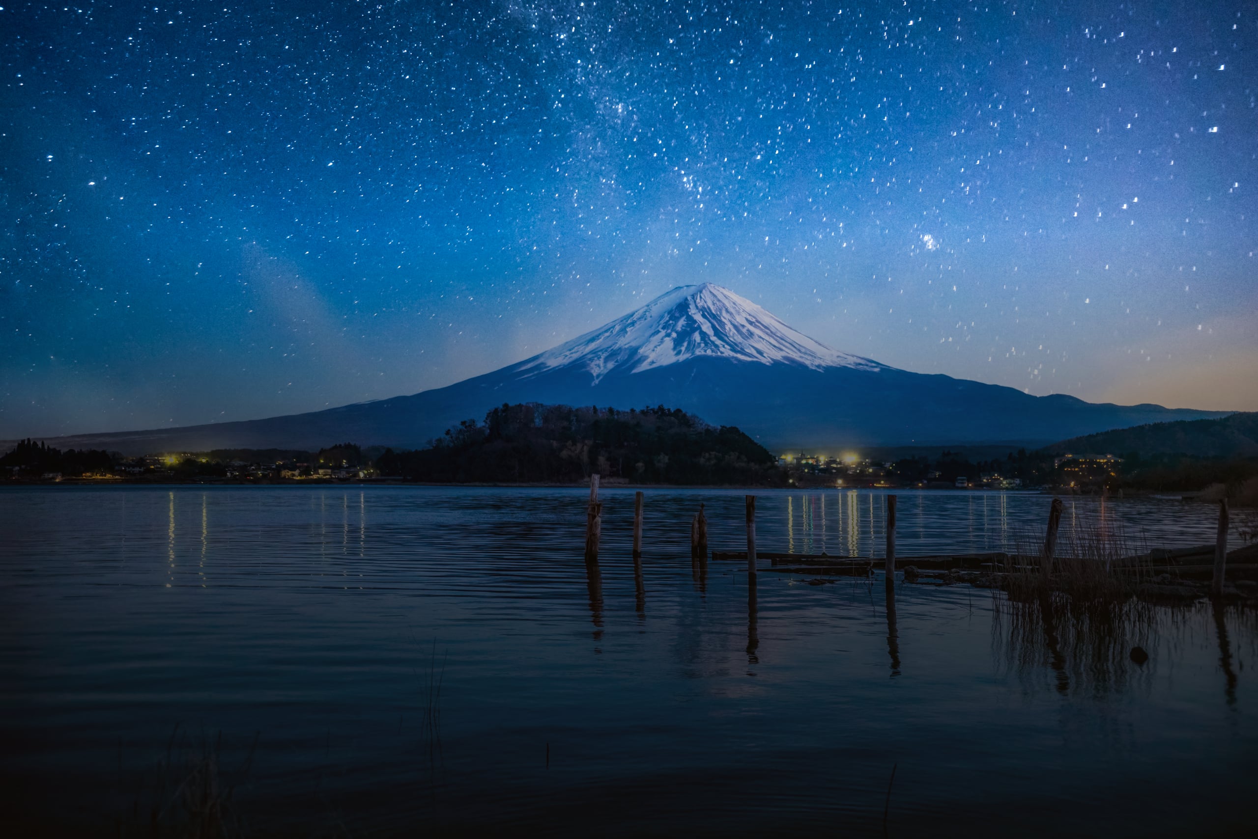 Mount Fuji under a sky of stars beyond Lake Kawaguchiko, old pier posts standing in the water