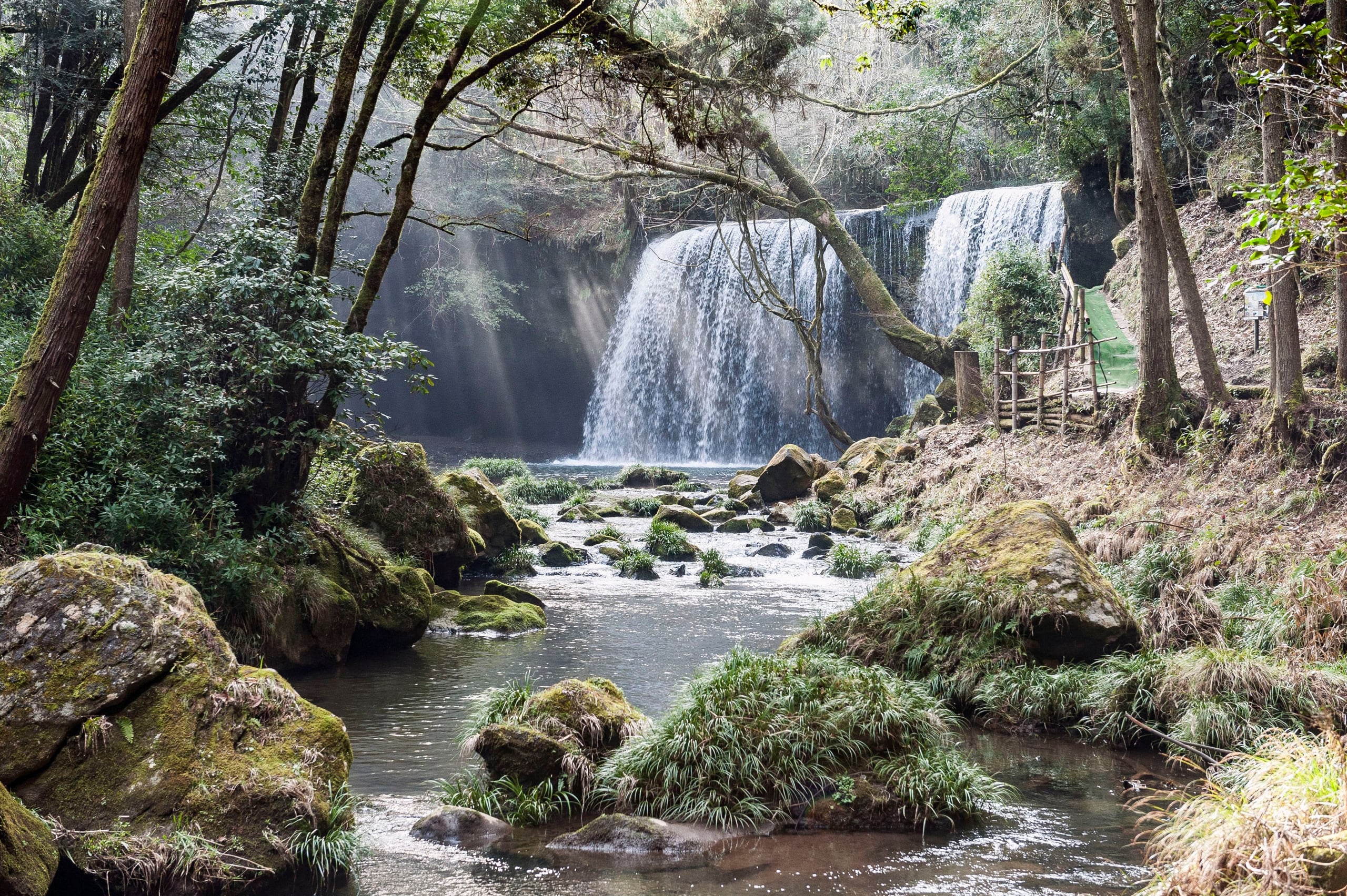 A wide curtain of water spilling over a mossy rock lip at Nabegataki Falls, Oguni, Kumamoto