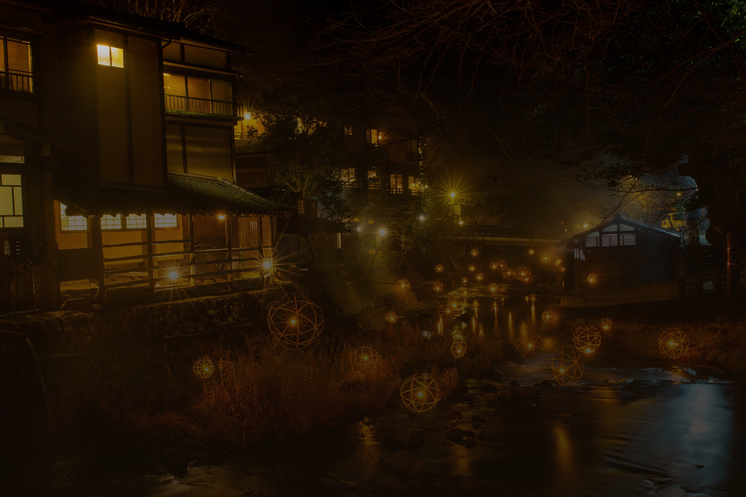 Wooden ryokan along the river at night, lanterns lit in the water and on the banks, Kurokawa Onsen
