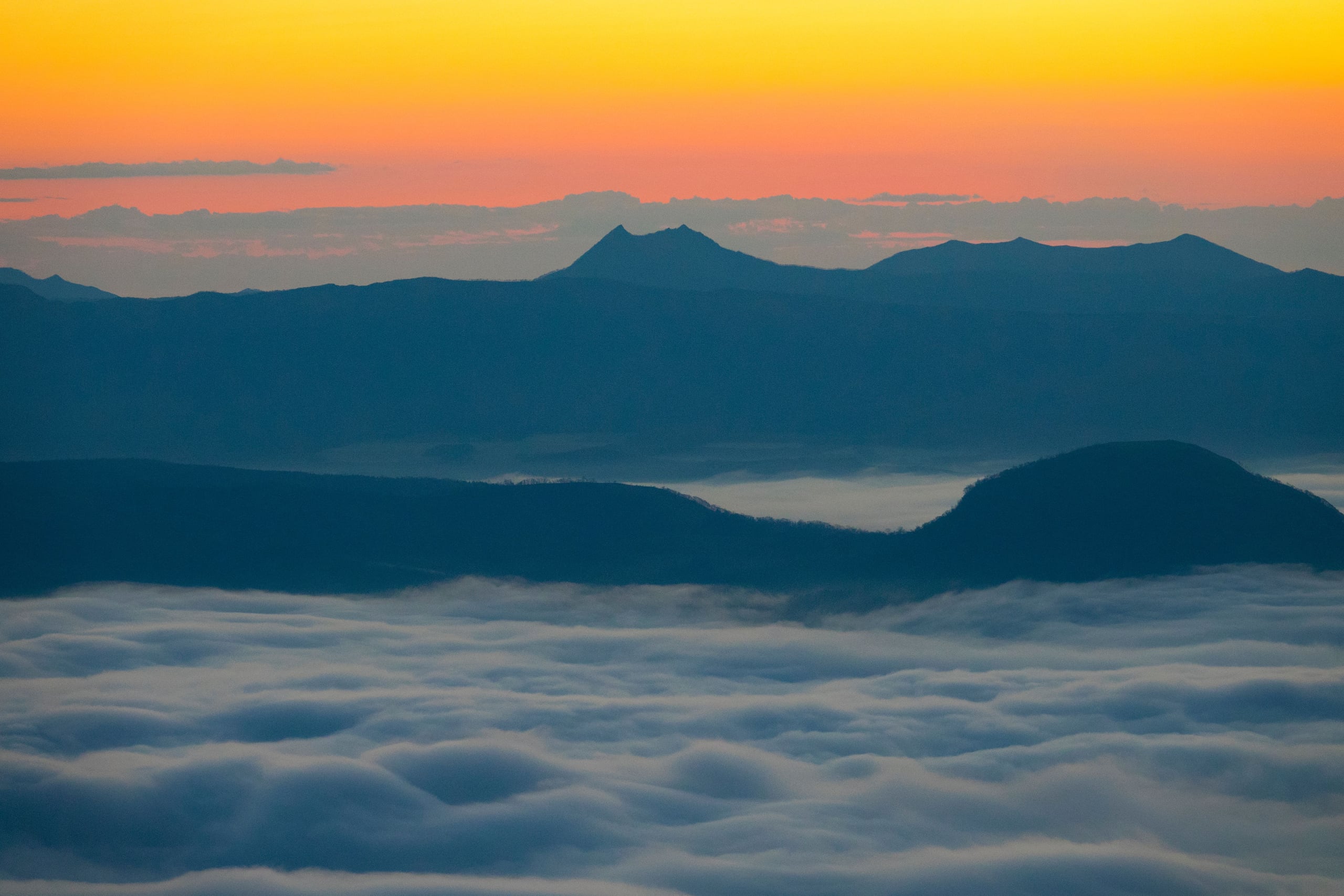 A sea of cloud filling a caldera basin, a mountain silhouetted beyond