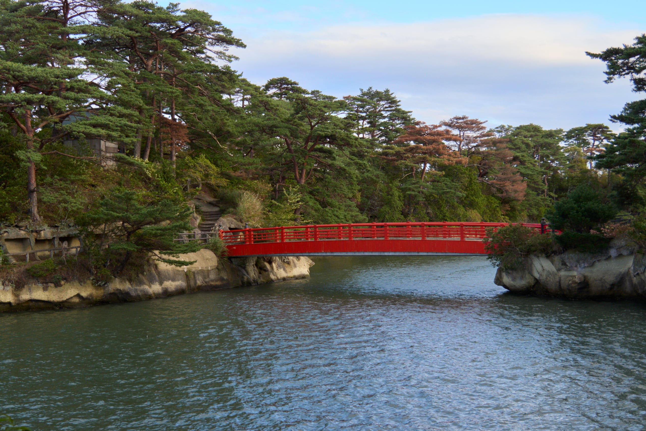 A red footbridge crossing between pine-covered rocky islets over the bay