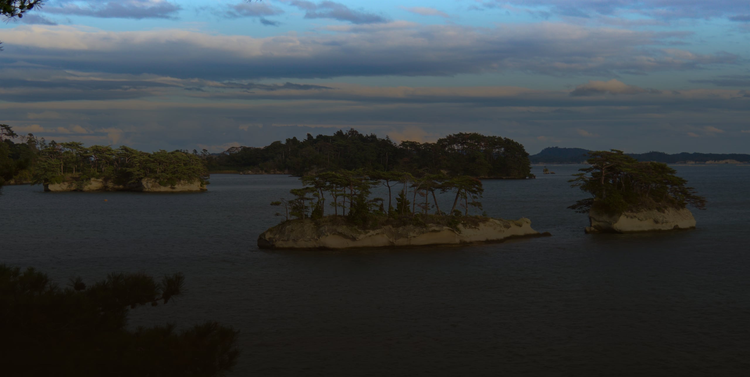 Pine-crowned islets of pale rock on the calm water of Matsushima Bay under a soft sky