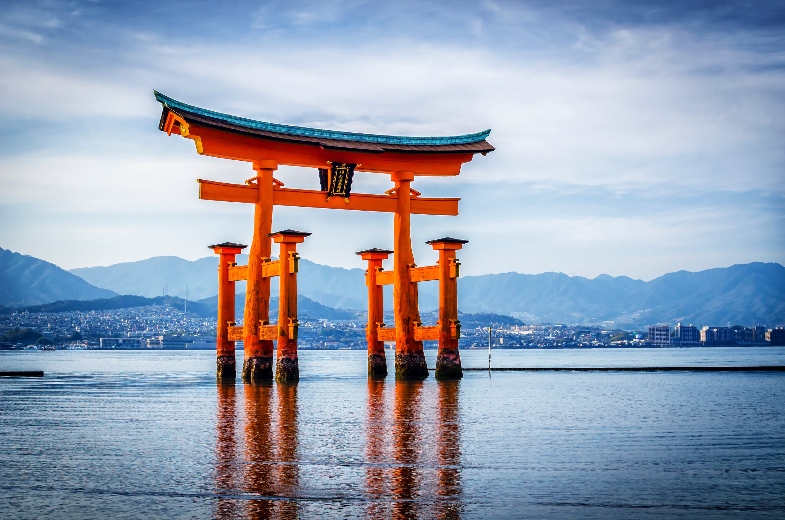 The orange great torii standing in shallow water under a pale sky, the mainland beyond