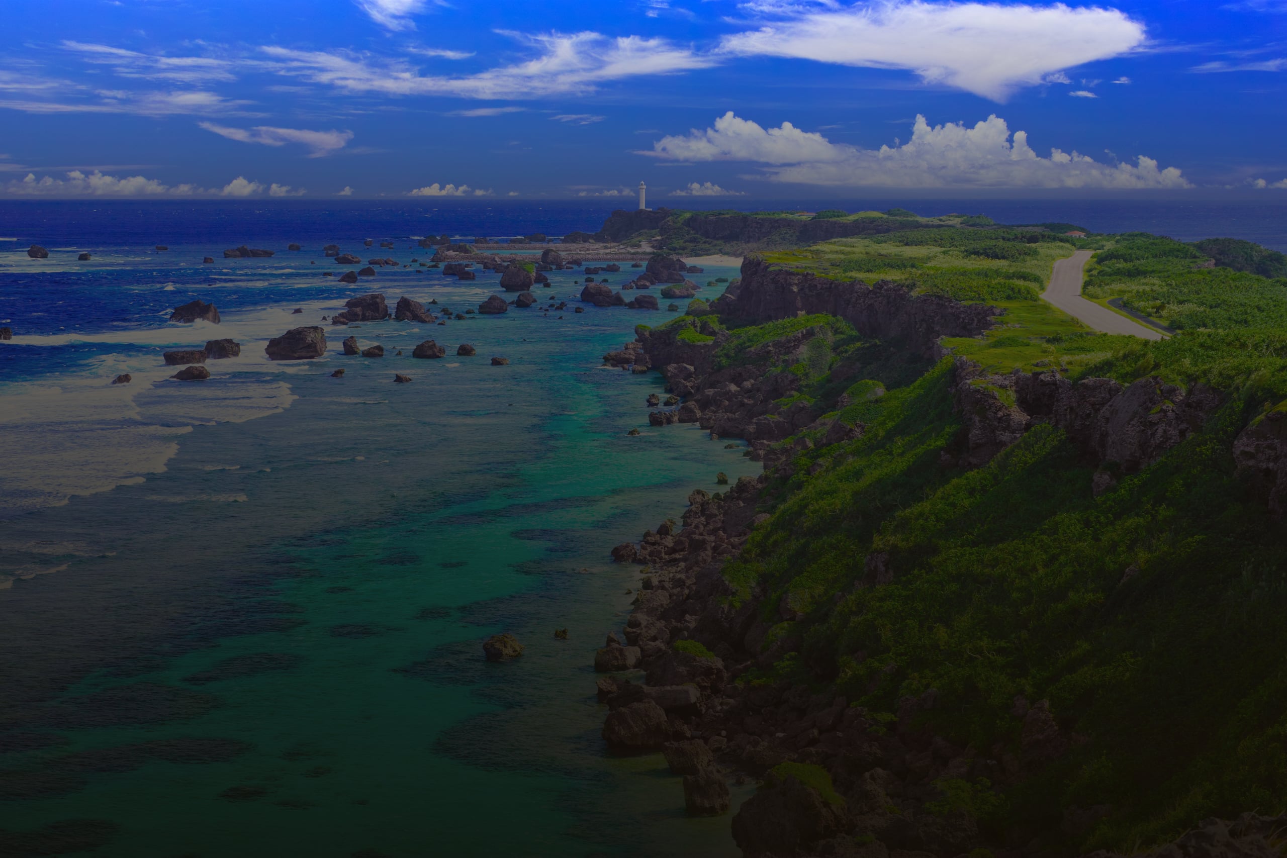 A green cape running out into a turquoise reef, a white lighthouse at its far end, Higashi-Hennazaki