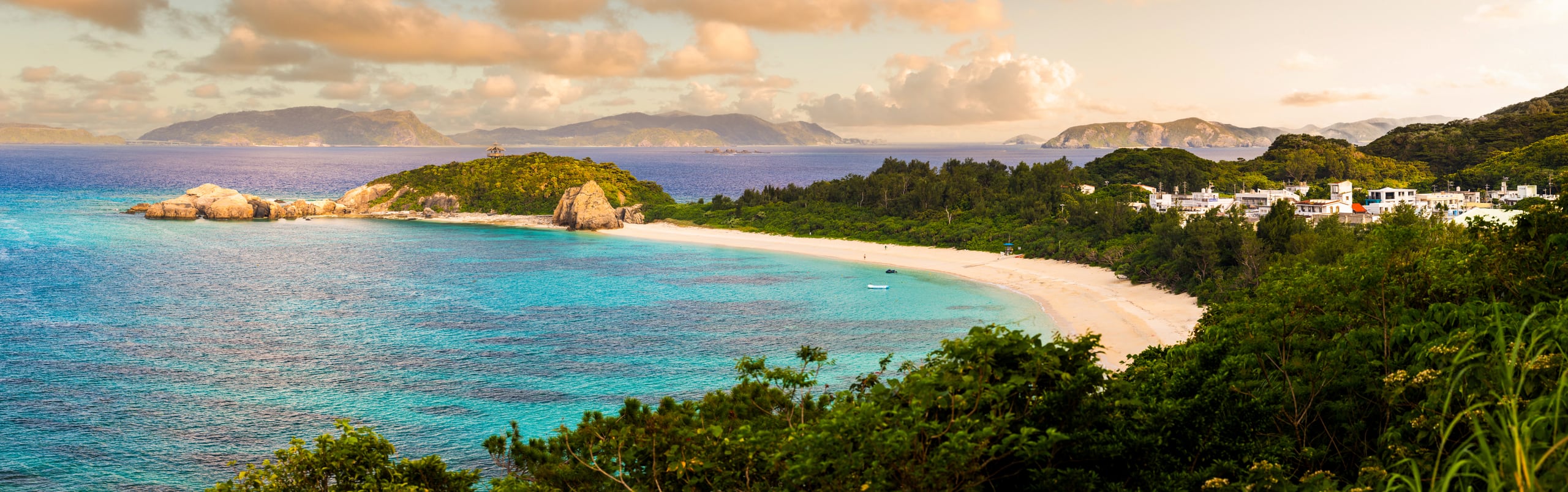 A crescent of white beach and turquoise water below green headlands, islands on the horizon, Tokashiki