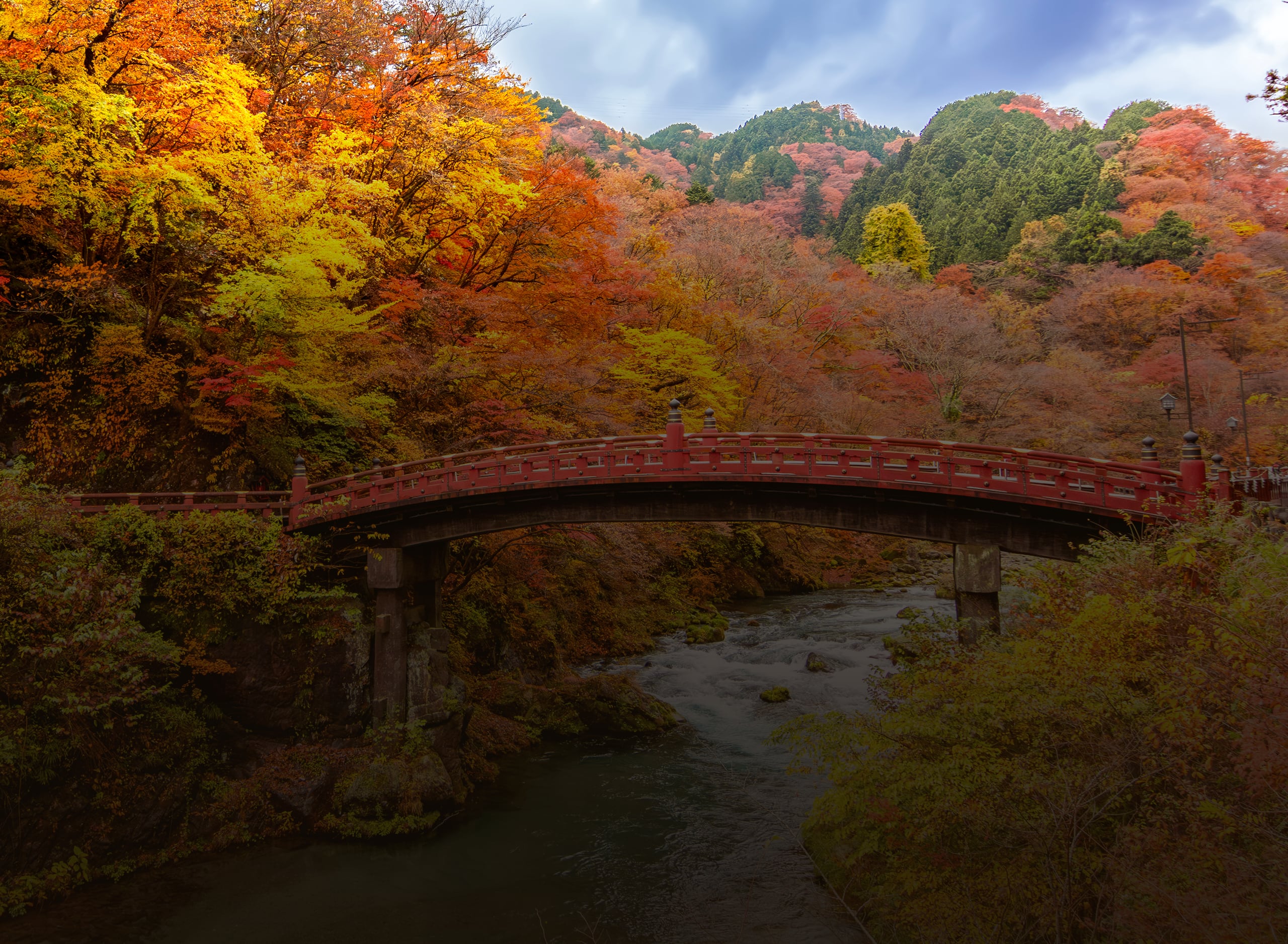 The vermilion Shinkyo bridge arching over a rocky river beneath red and gold maples, Nikko