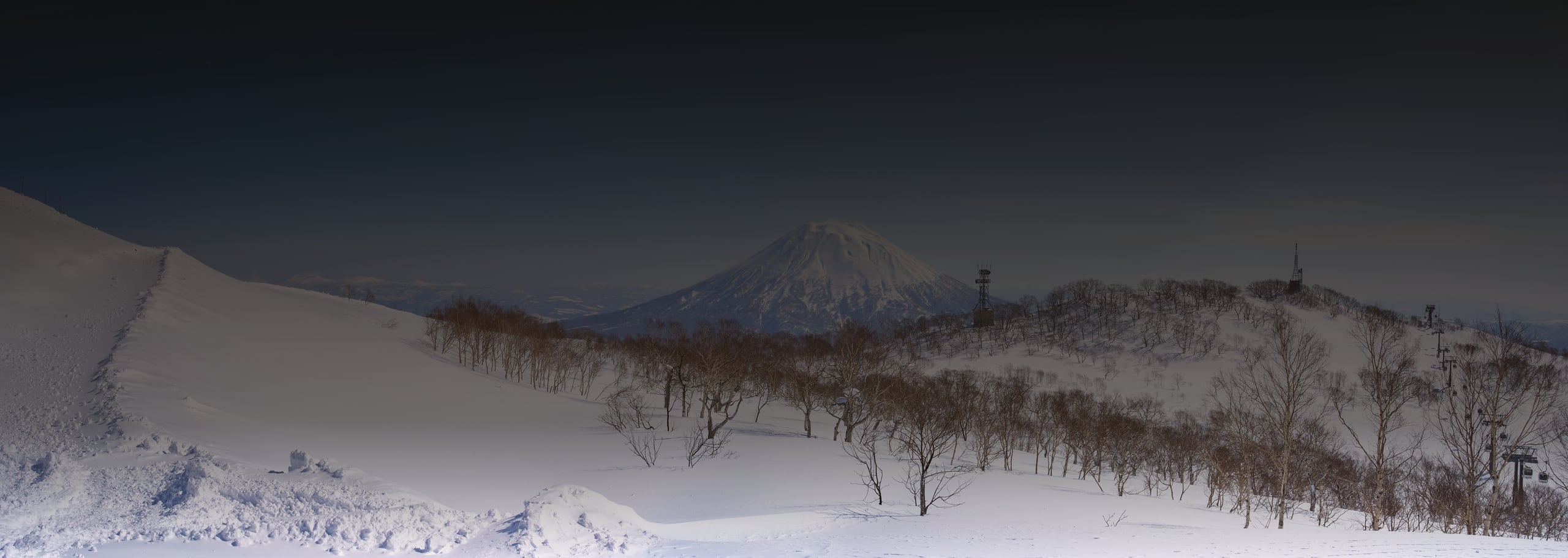 The snow-covered cone of Mount Yotei beyond snowfields and bare trees under a clear blue sky