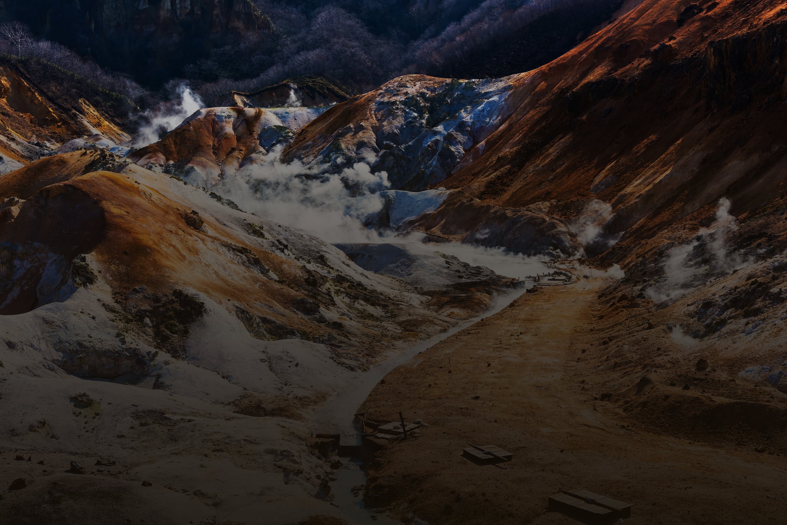The steaming volcanic valley of Jigokudani seen from above, orange and white mineral slopes and a path below