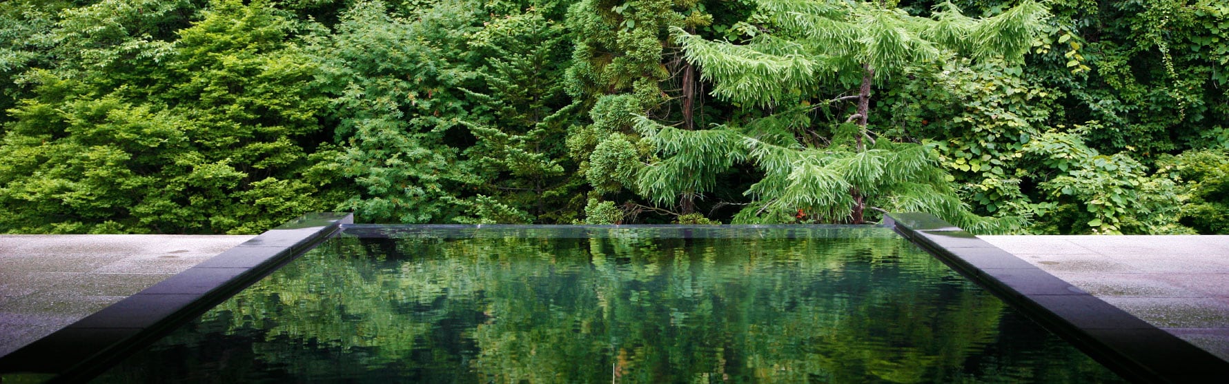 An open-air onsen at Takinoya edged with rock, the trees reflected in the water