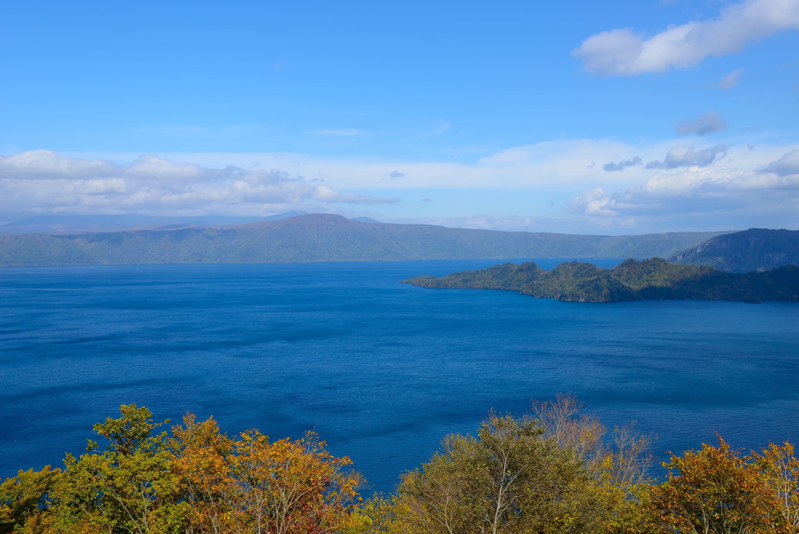 Lake Towada's deep blue water under a wide sky, a forested peninsula reaching into it