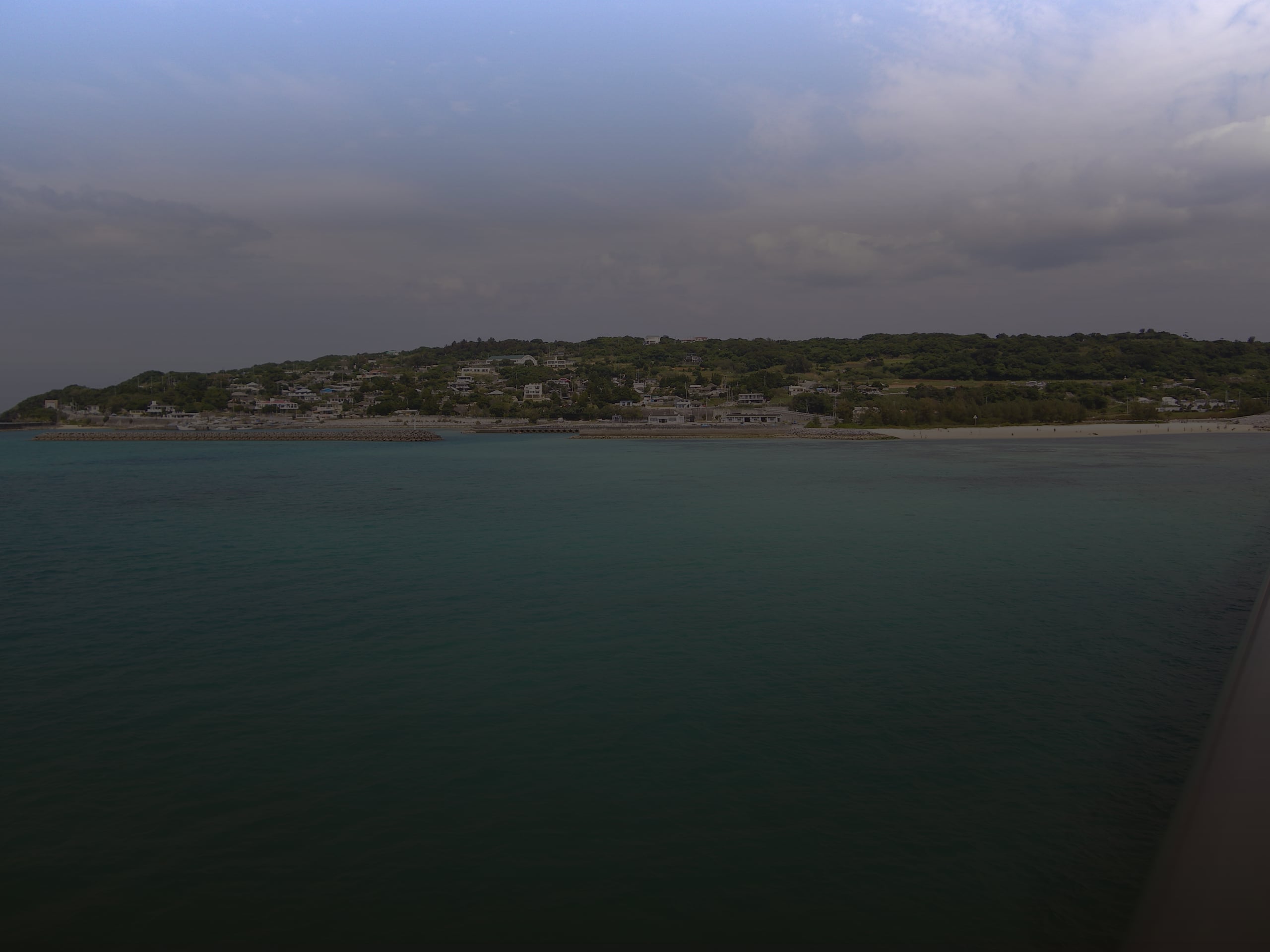 Kouri Island low on the horizon across clear turquoise shallows, seen from the Kouri Bridge