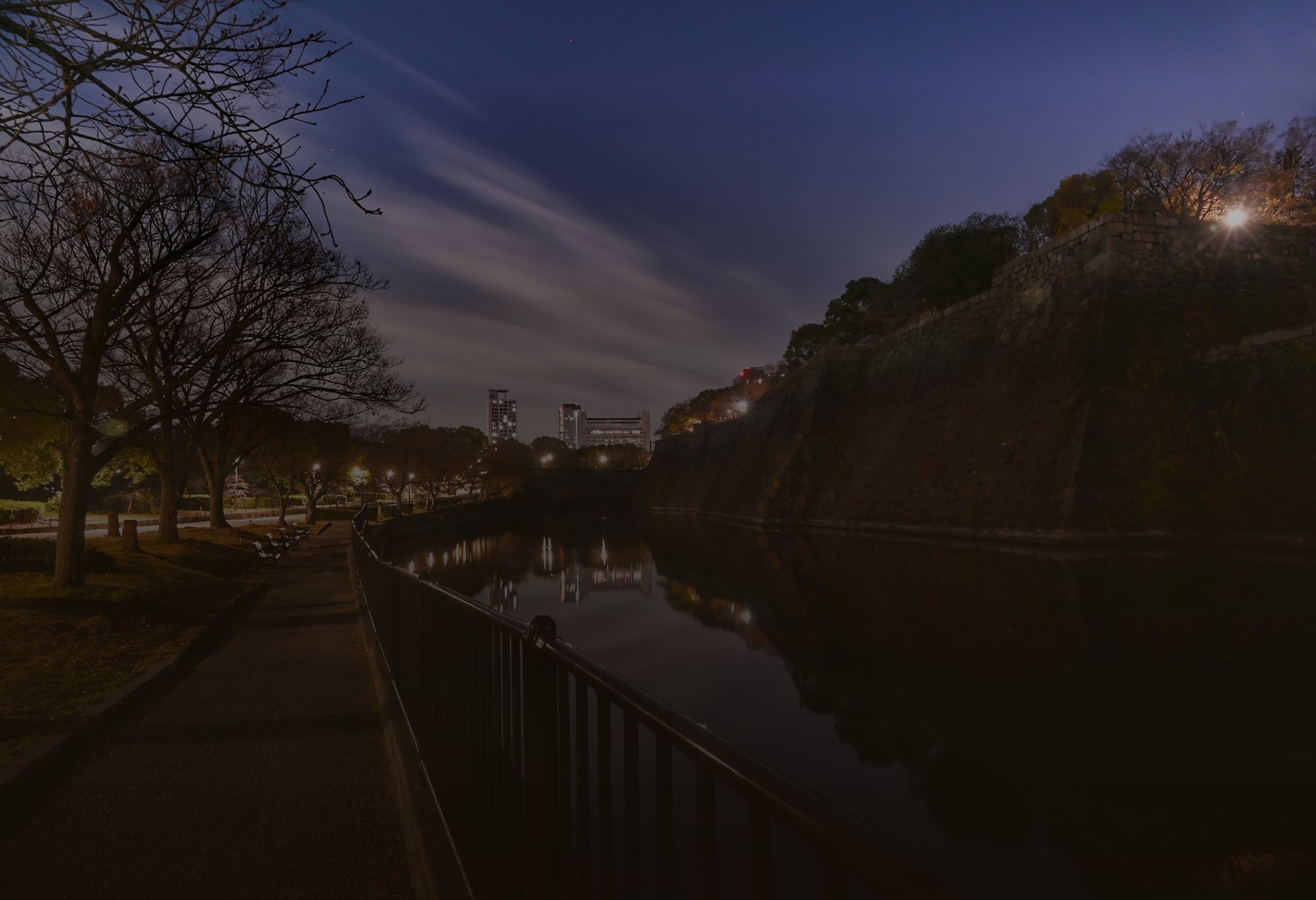 The stone walls of Osaka Castle and a riverside path beside the still moat at night