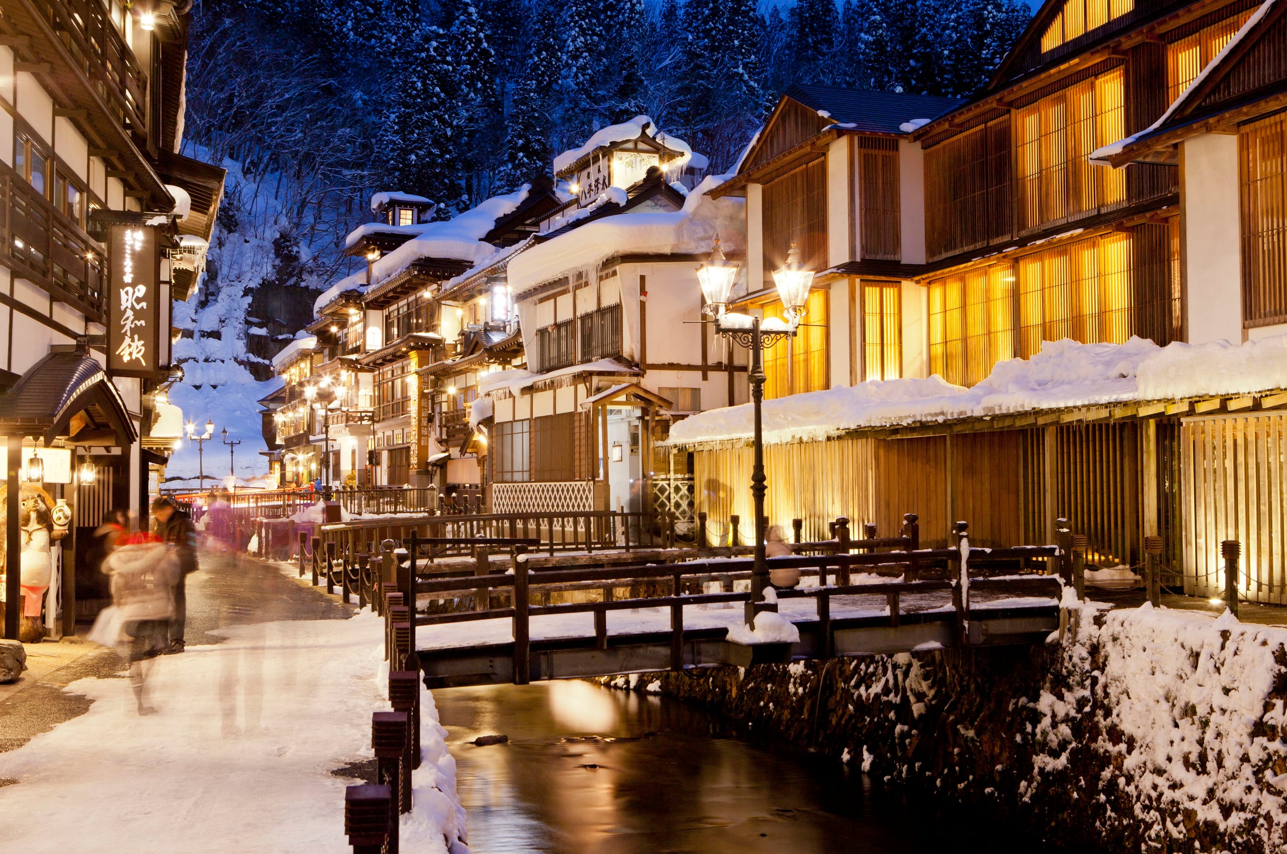 The wooden inns of Ginzan Onsen under snow at blue hour, lamps lit along the river