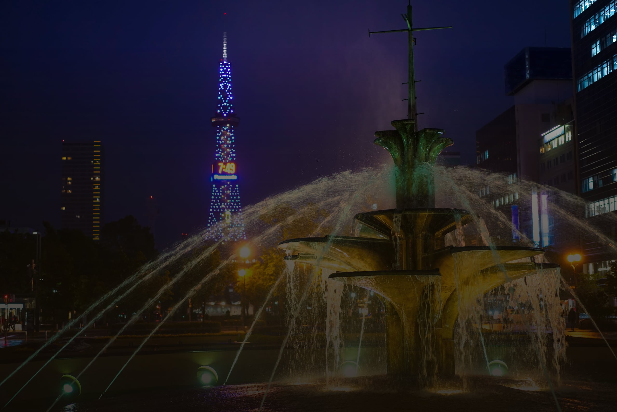 A tiered fountain lit at night in Odori Park, the Sapporo television tower glowing blue behind it