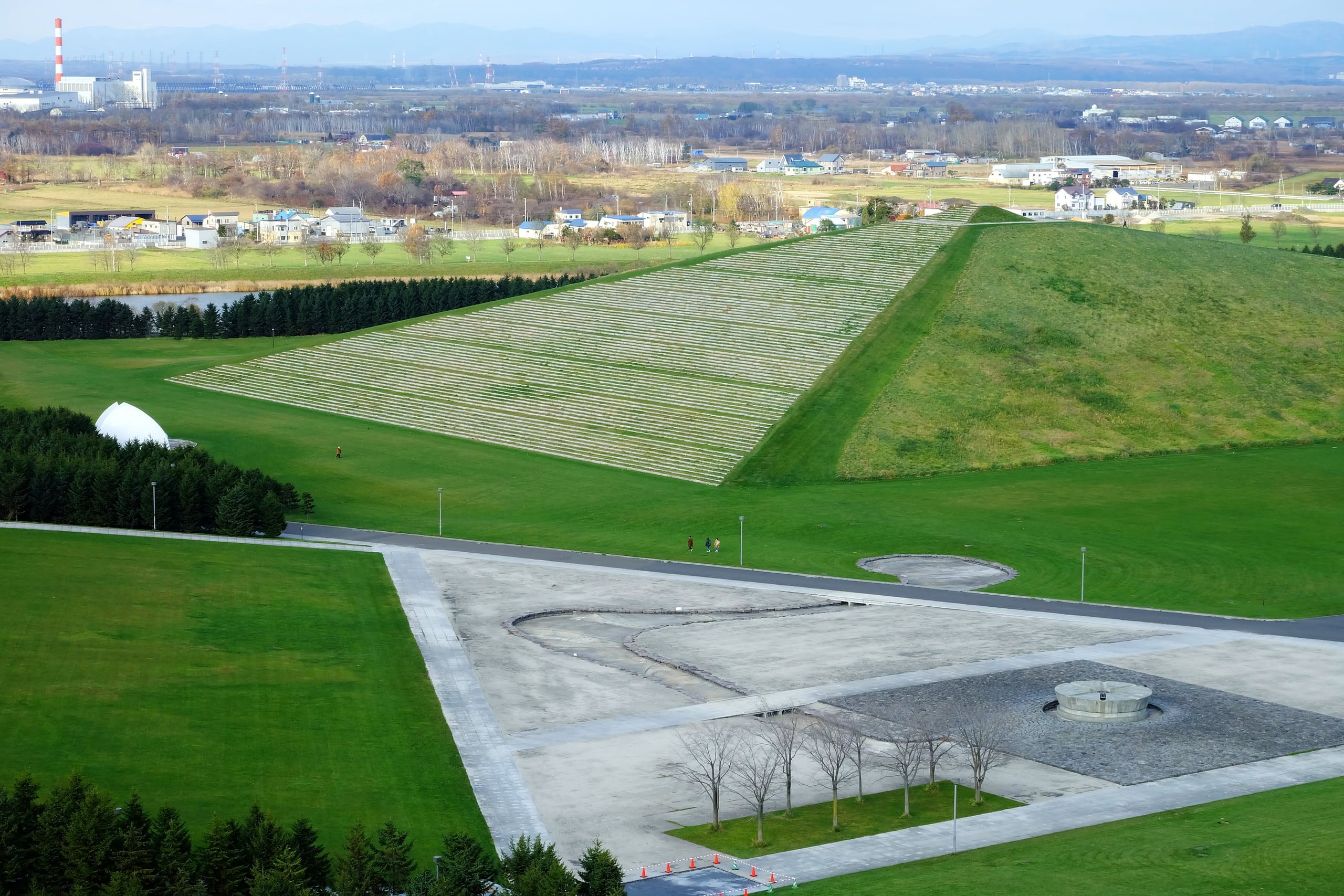The grass pyramid of Moere-yama and the stone paths of Moerenuma Park seen from above, the city beyond