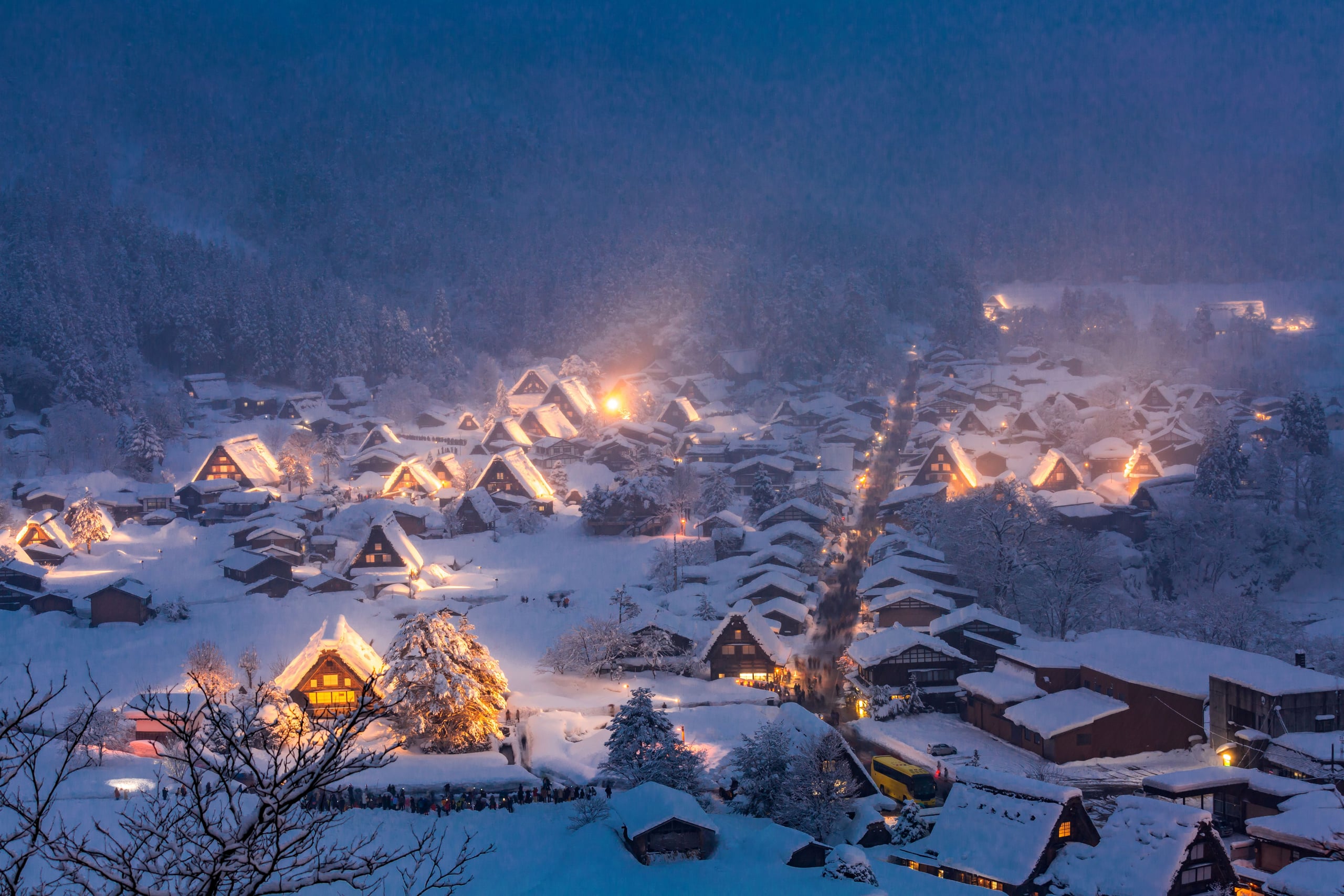 The snow-covered thatched farmhouses of Ogimachi lit at blue hour, seen from the Shiroyama viewpoint, Shirakawa-go