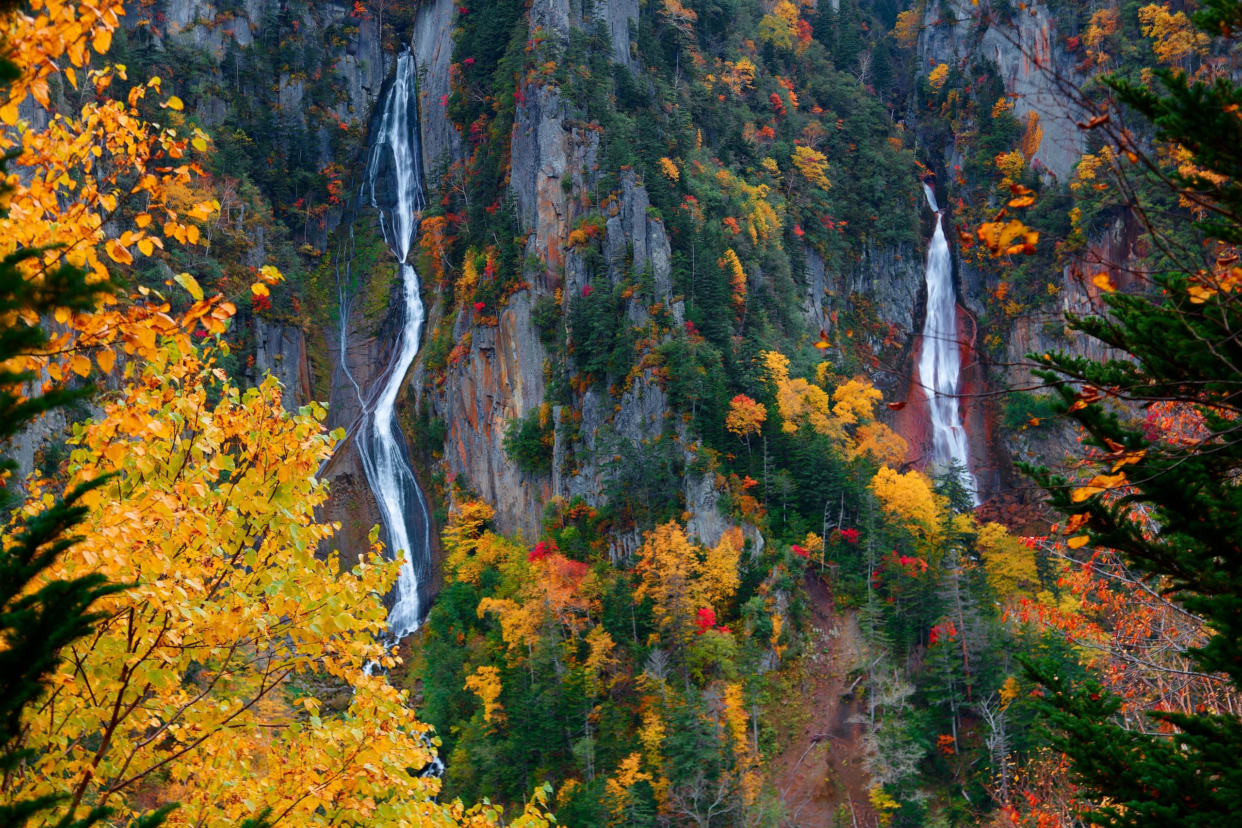 Two waterfalls, Ginga and Ryusei, cascading down a rugged grey cliff in autumn colour, Sounkyo Gorge