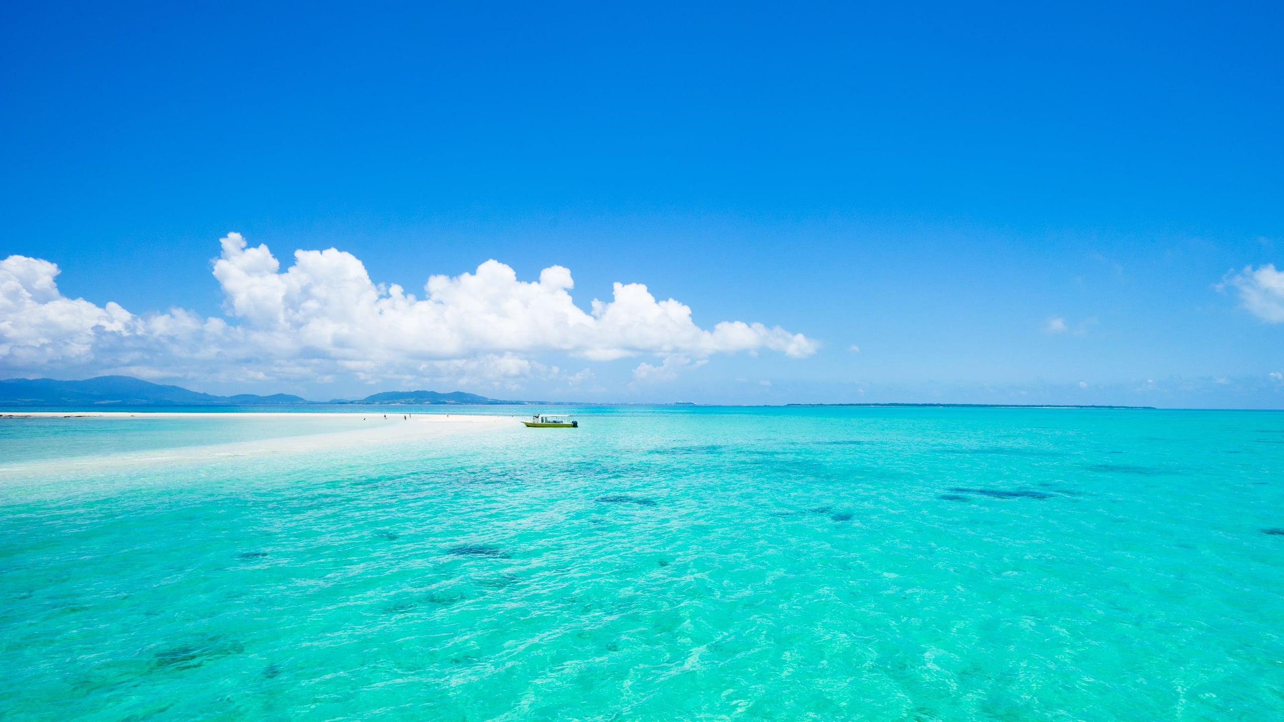 A small boat moored beside a white sand cay in the turquoise water of Sekisei Lagoon