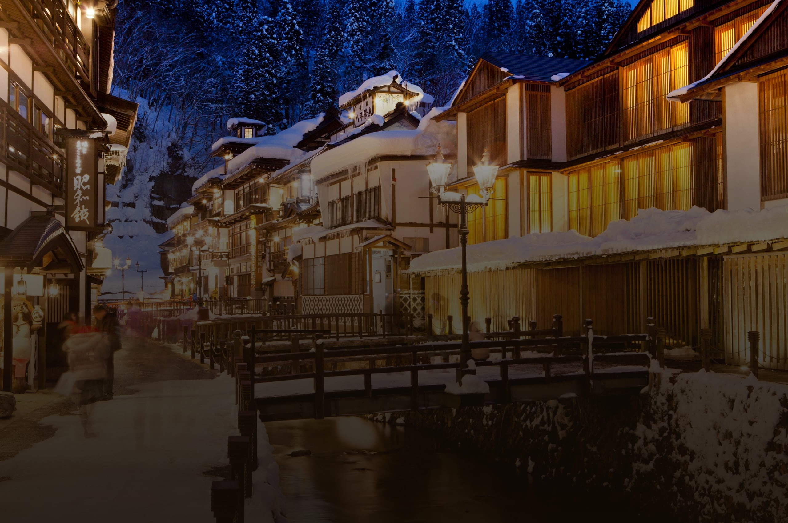 The wooden inns of Ginzan Onsen under snow at blue hour, lamps lit along the river