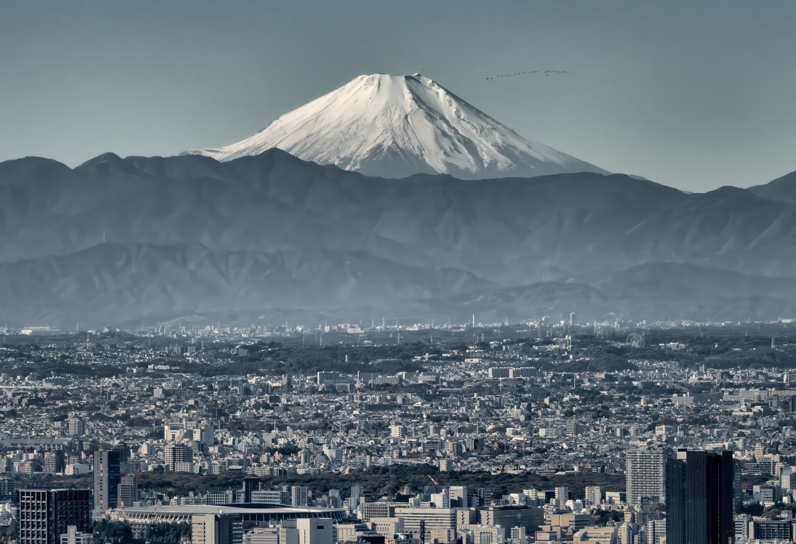 Snow-capped Mount Fuji rising above the mountains beyond the rooftops of Tokyo