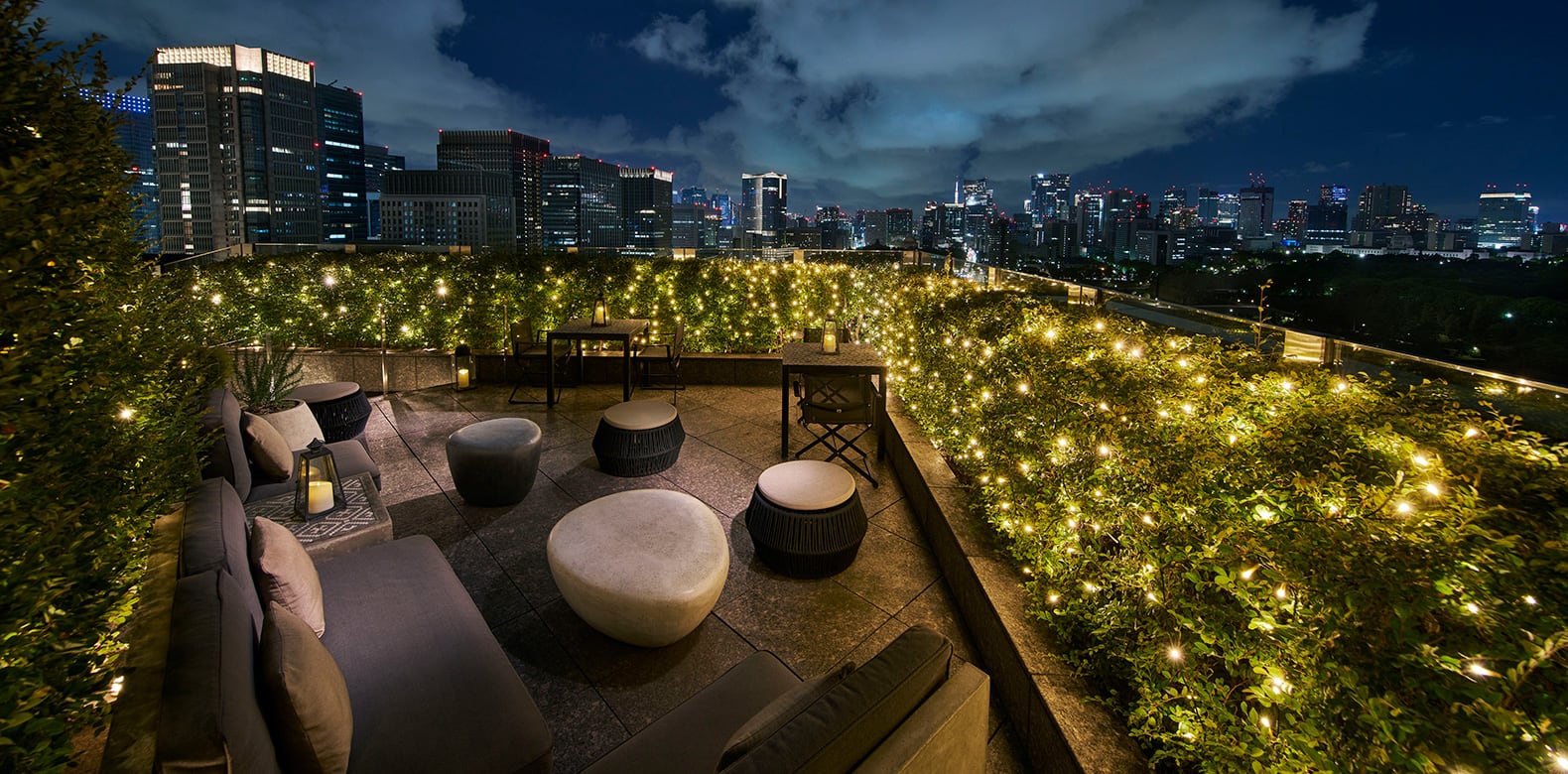 A lit garden terrace with low seats above the towers of Marunouchi at night, Palace Hotel Tokyo