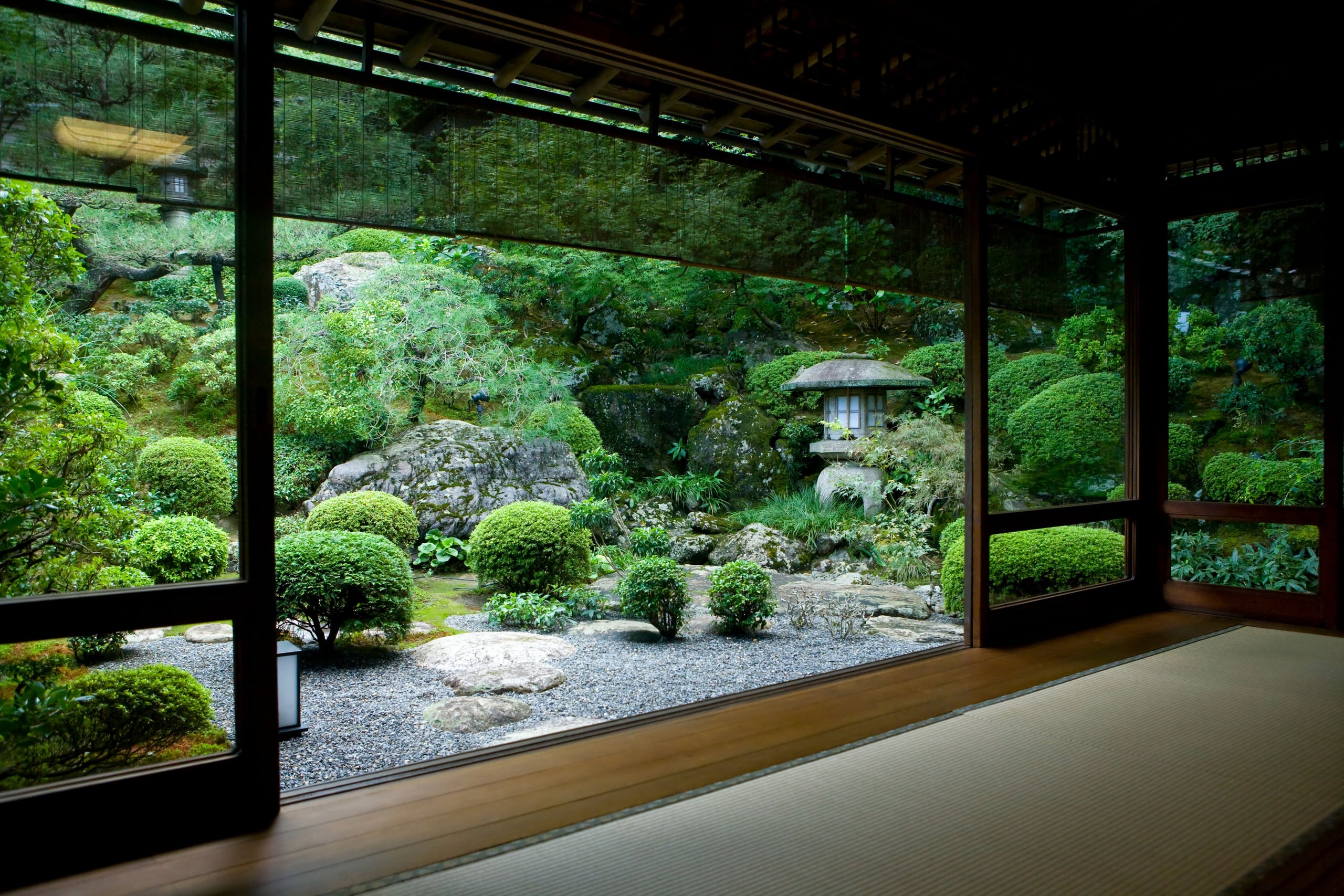 A tatami room opening through shoji doors onto a clipped garden with a stone lantern, in the green of summer