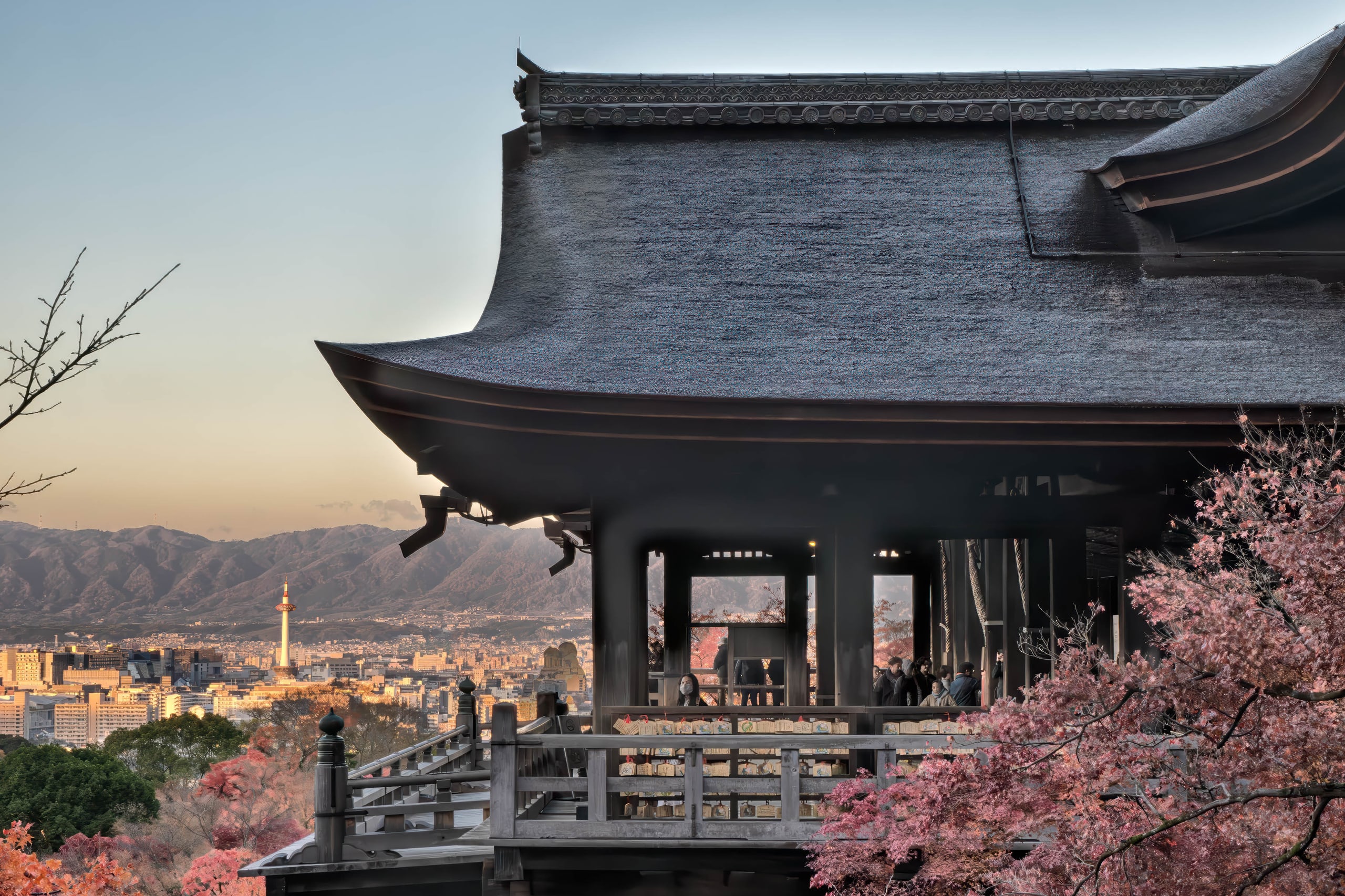 The wooden stage of Kiyomizu-dera beneath its great roof, maples below and the city of Kyoto beyond, at dusk