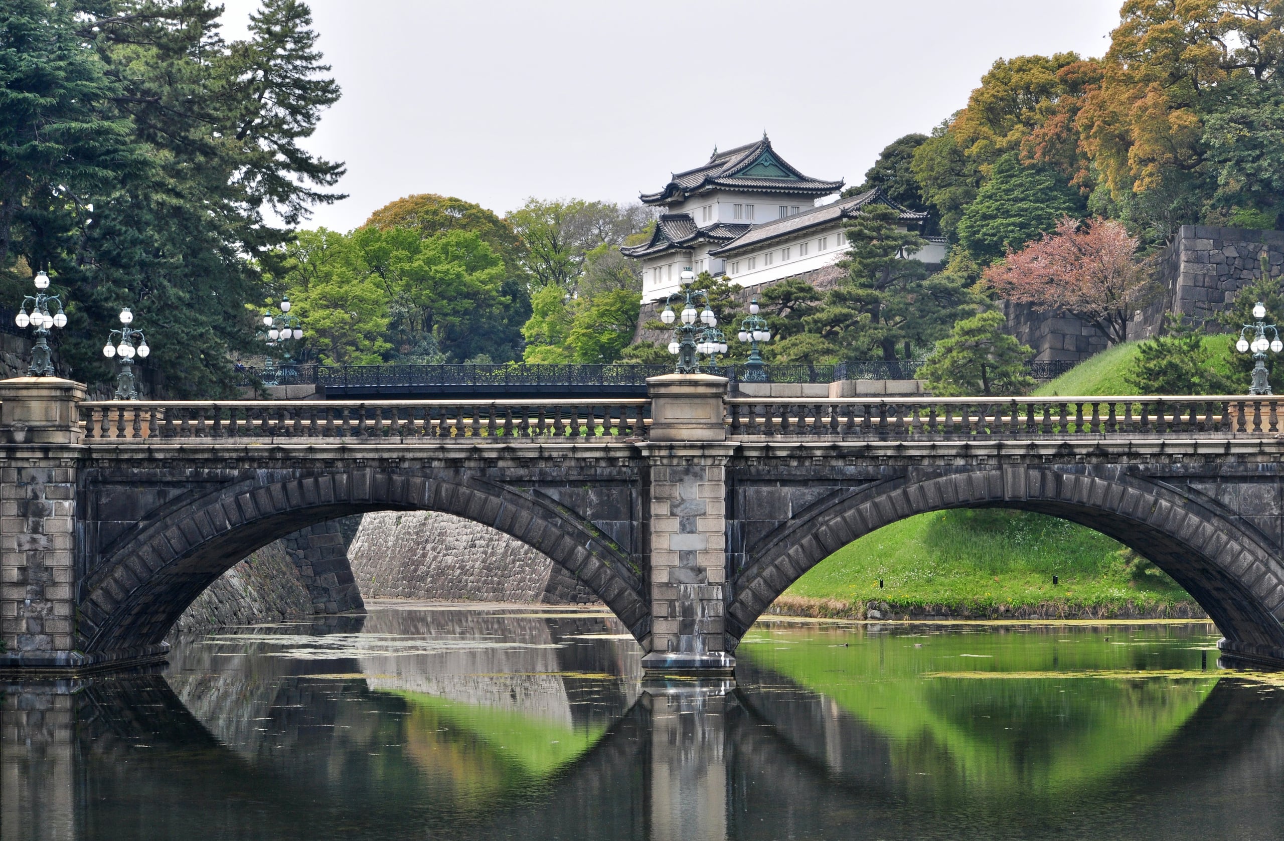 The double-arched stone bridge of Nijubashi reflected in the palace moat, the white Fushimi watchtower above it among the pines