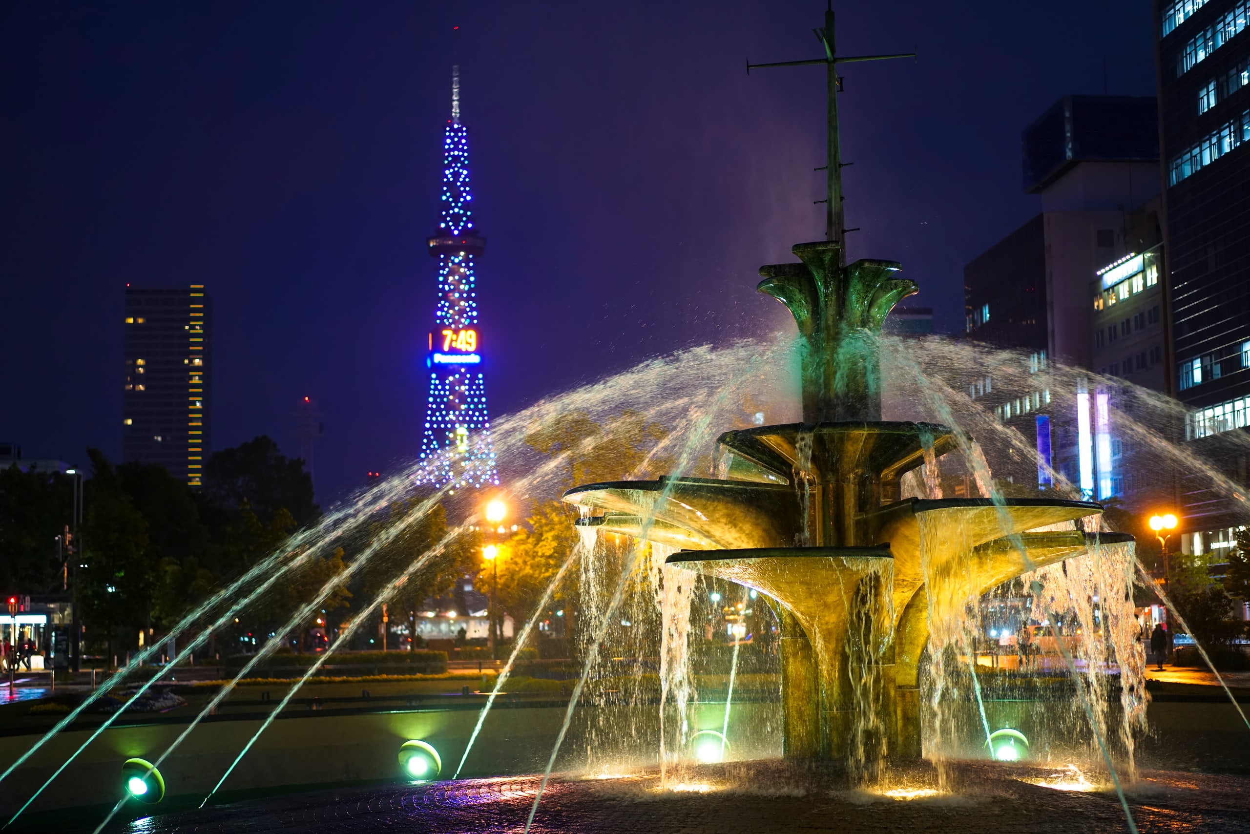 The fountain in Odori Park lit at night, the Sapporo TV Tower rising behind it