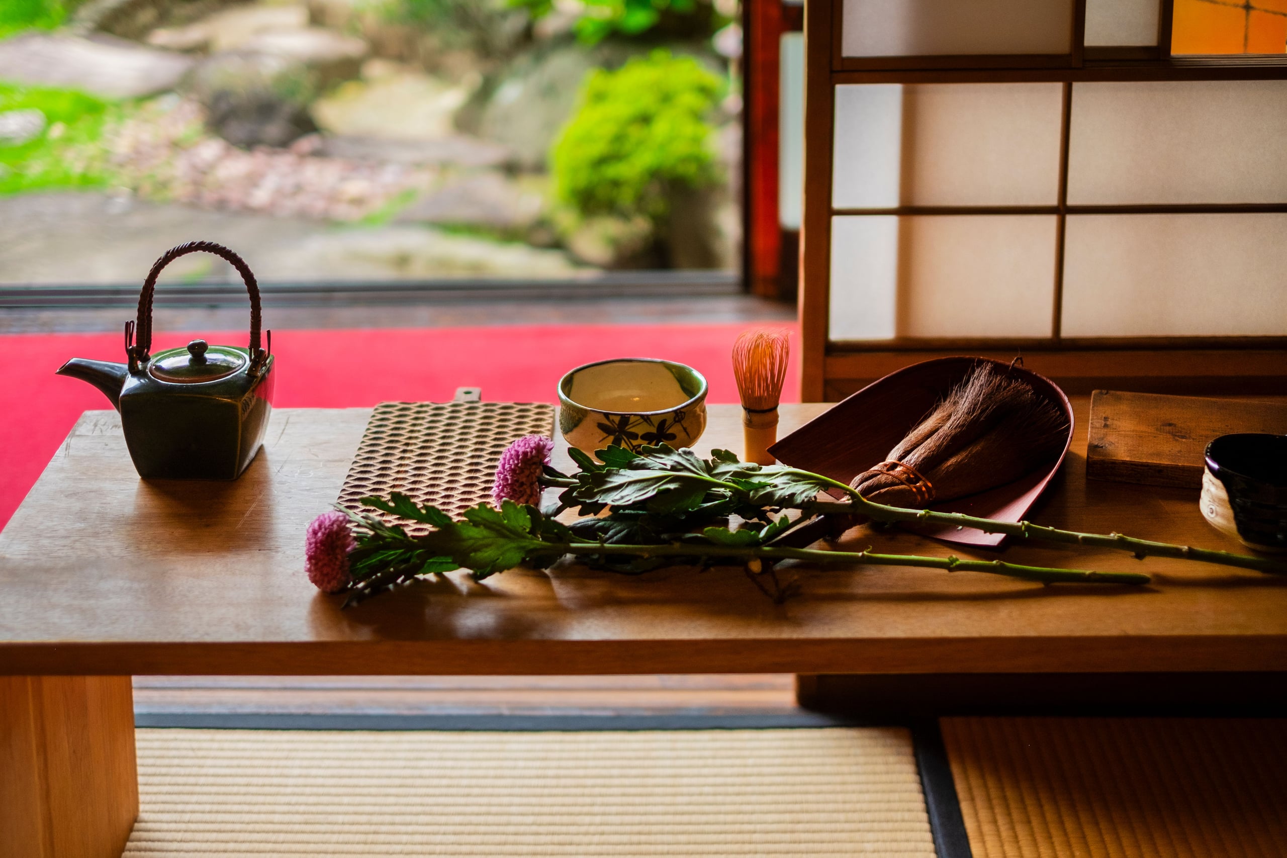A cast-iron teapot and glazed tea bowls on tatami beside open shoji and a garden